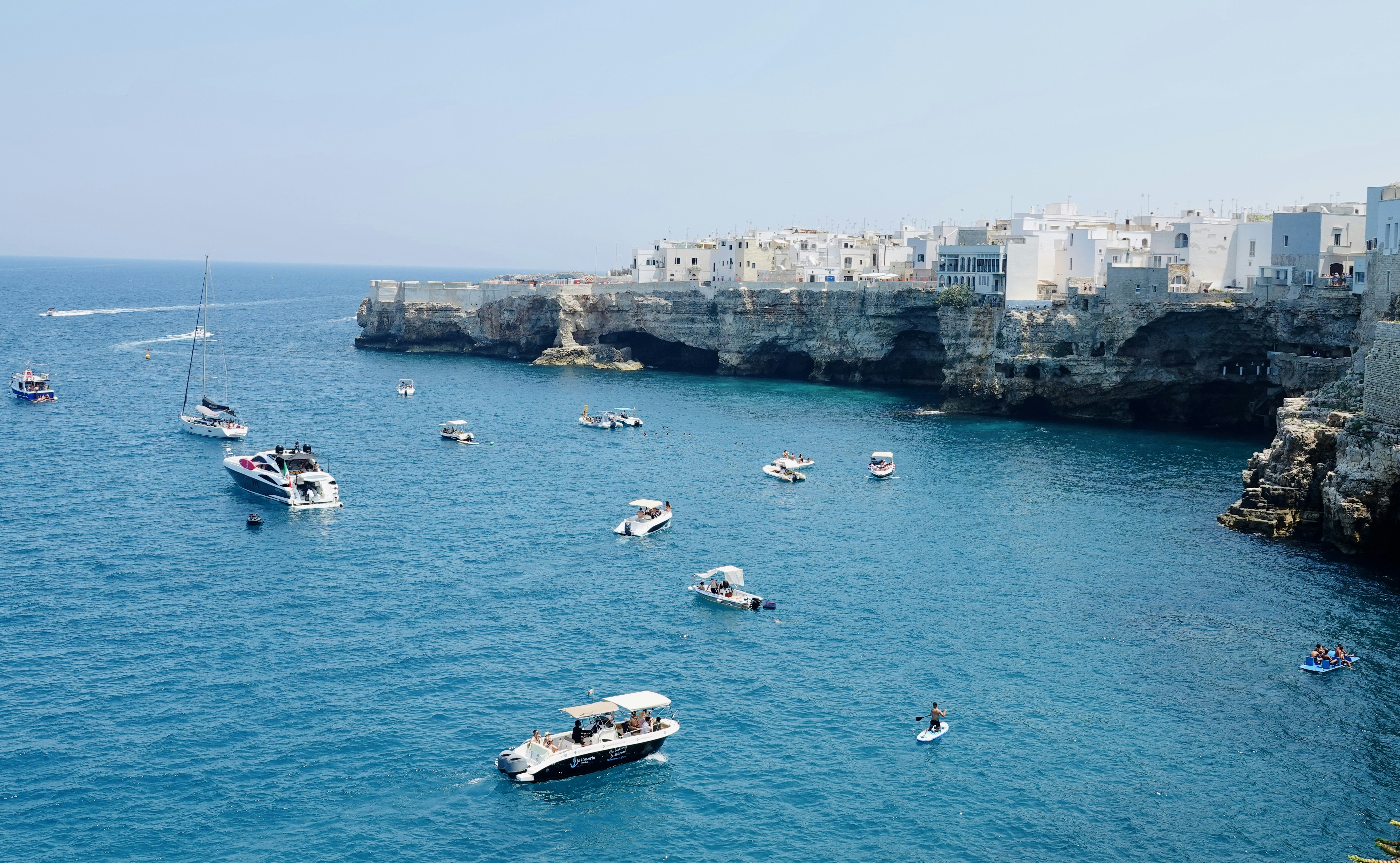 Boats on clear turquoise water below the white clifftop old town of Polignano a Mare, Puglia