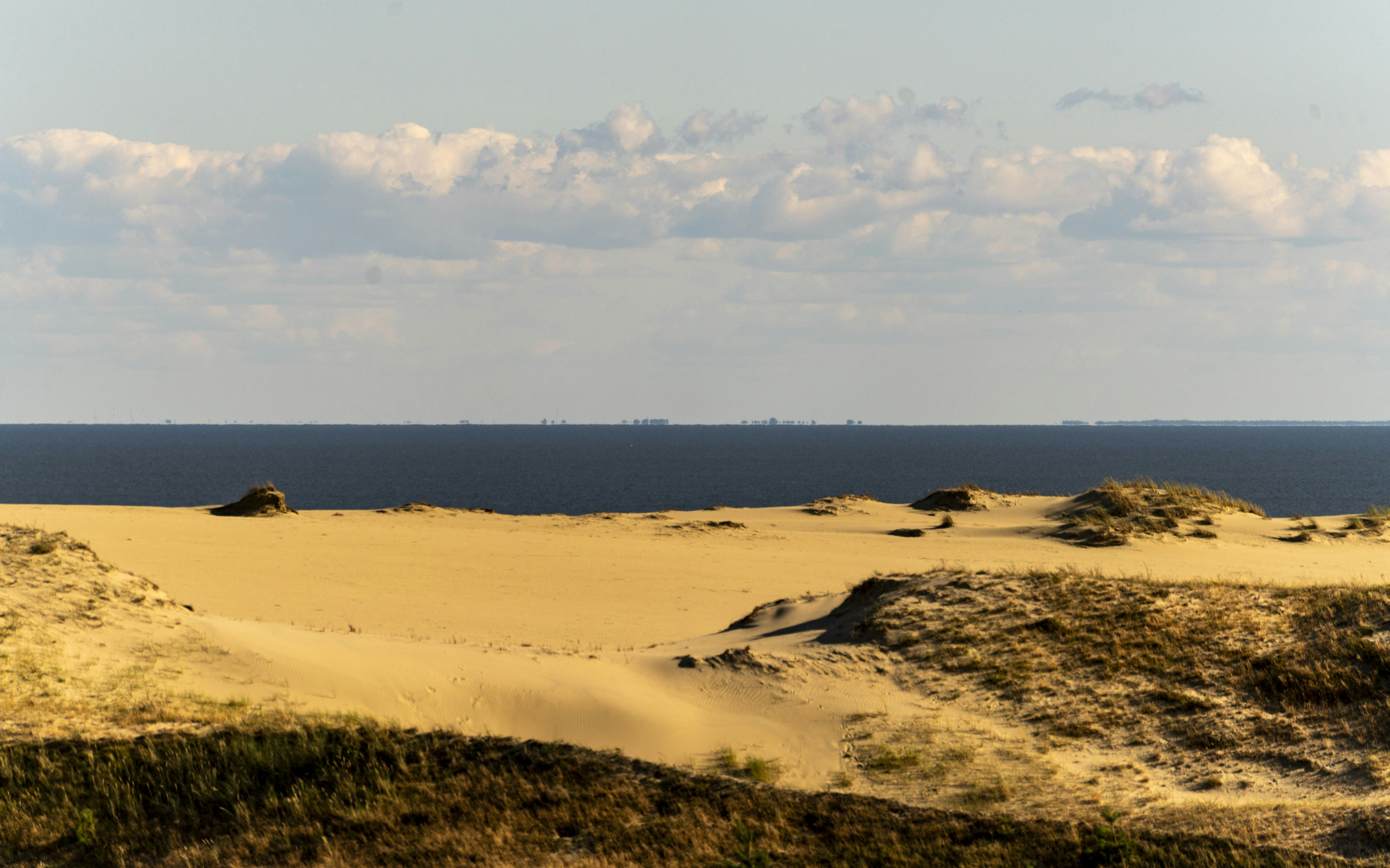 Golden sand dunes under a blue sky with scattered clouds above a dark sea