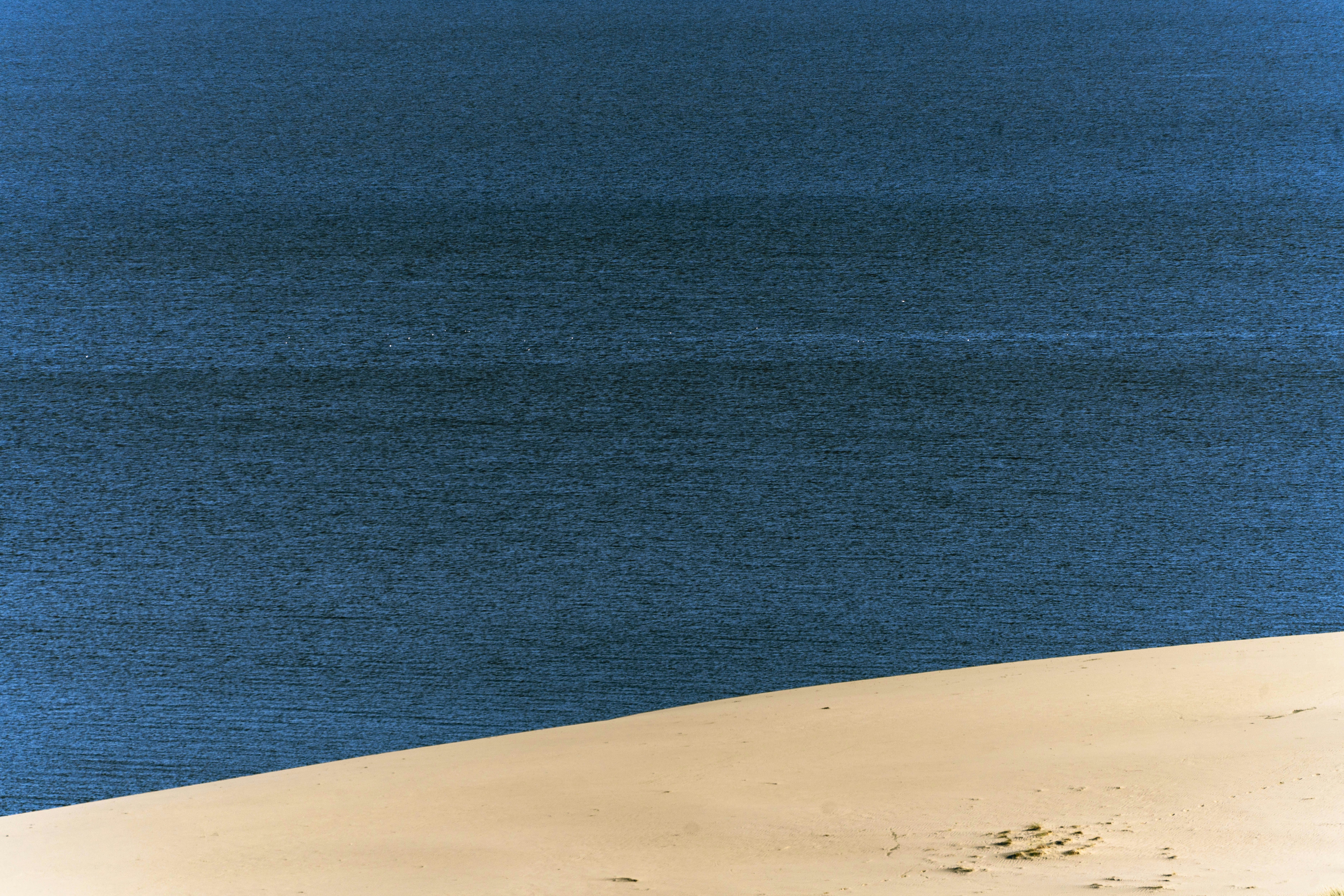 A diagonal view of a sandy dune meeting the deep blue water of the sea