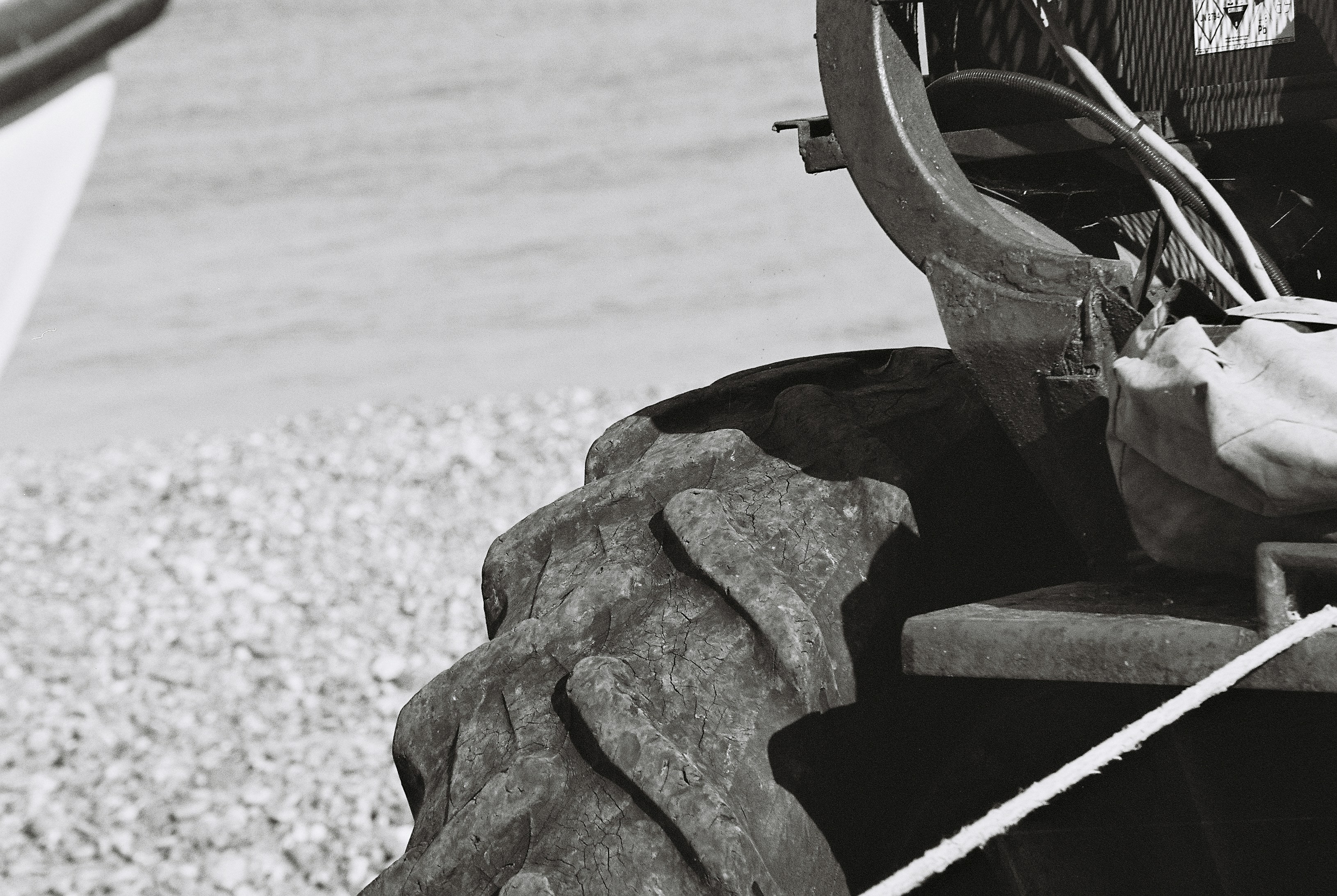 A weathered tractor tyre with deep tread beside a pebble beach