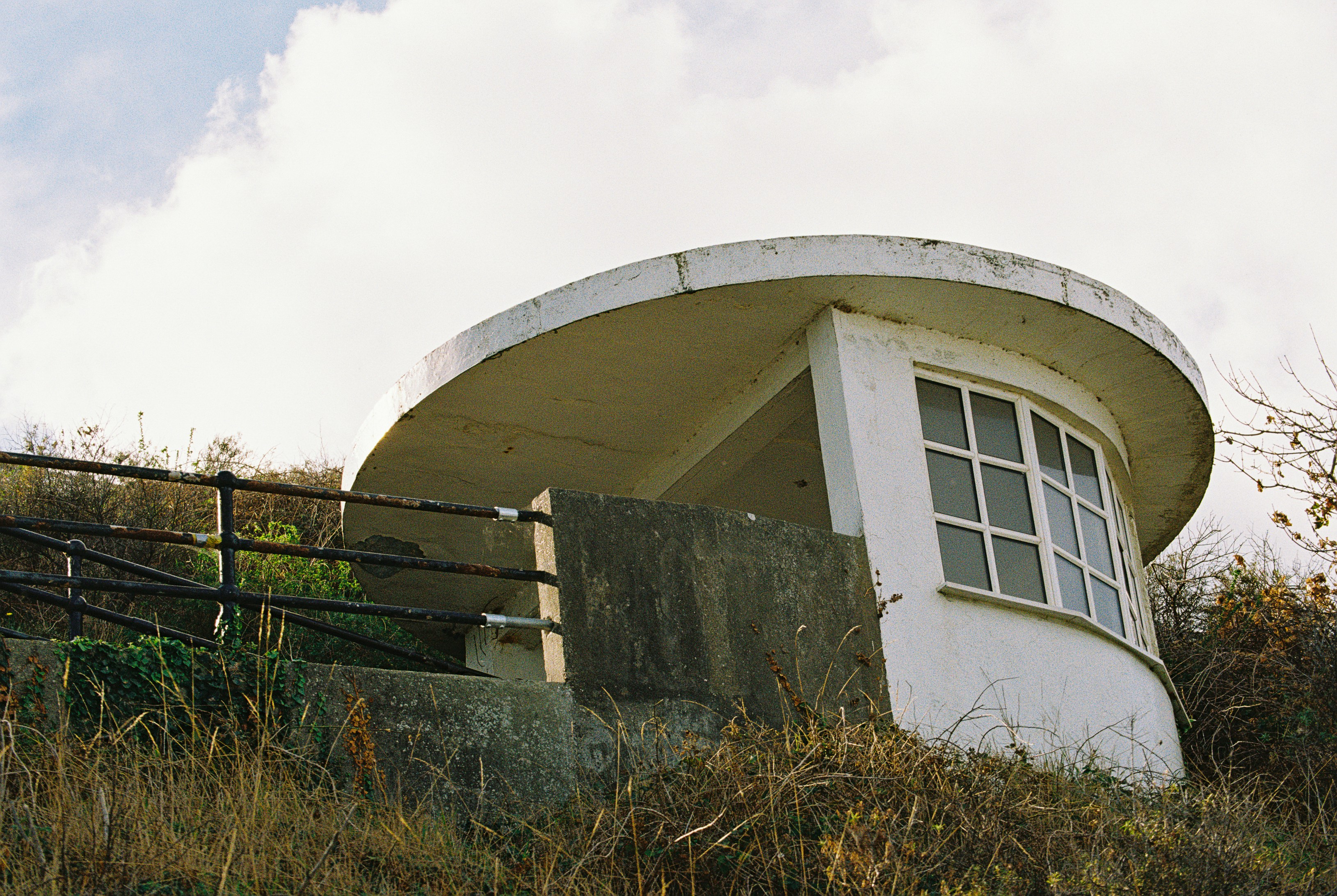 A white concrete shelter with a curved roof on a grassy slope
