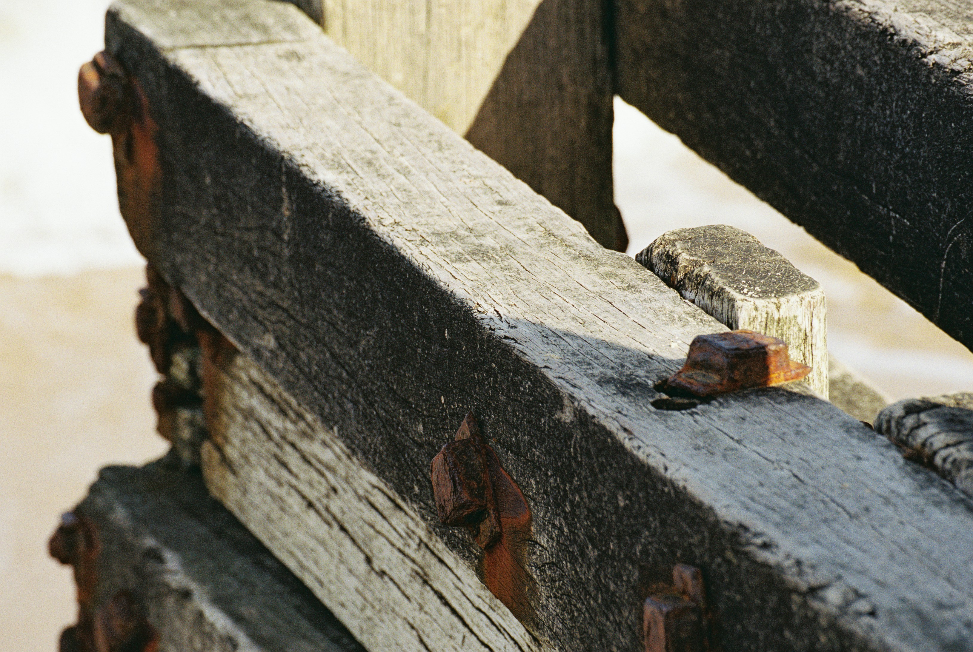 A weathered grey timber beam with rusted iron bolts in bright sunlight