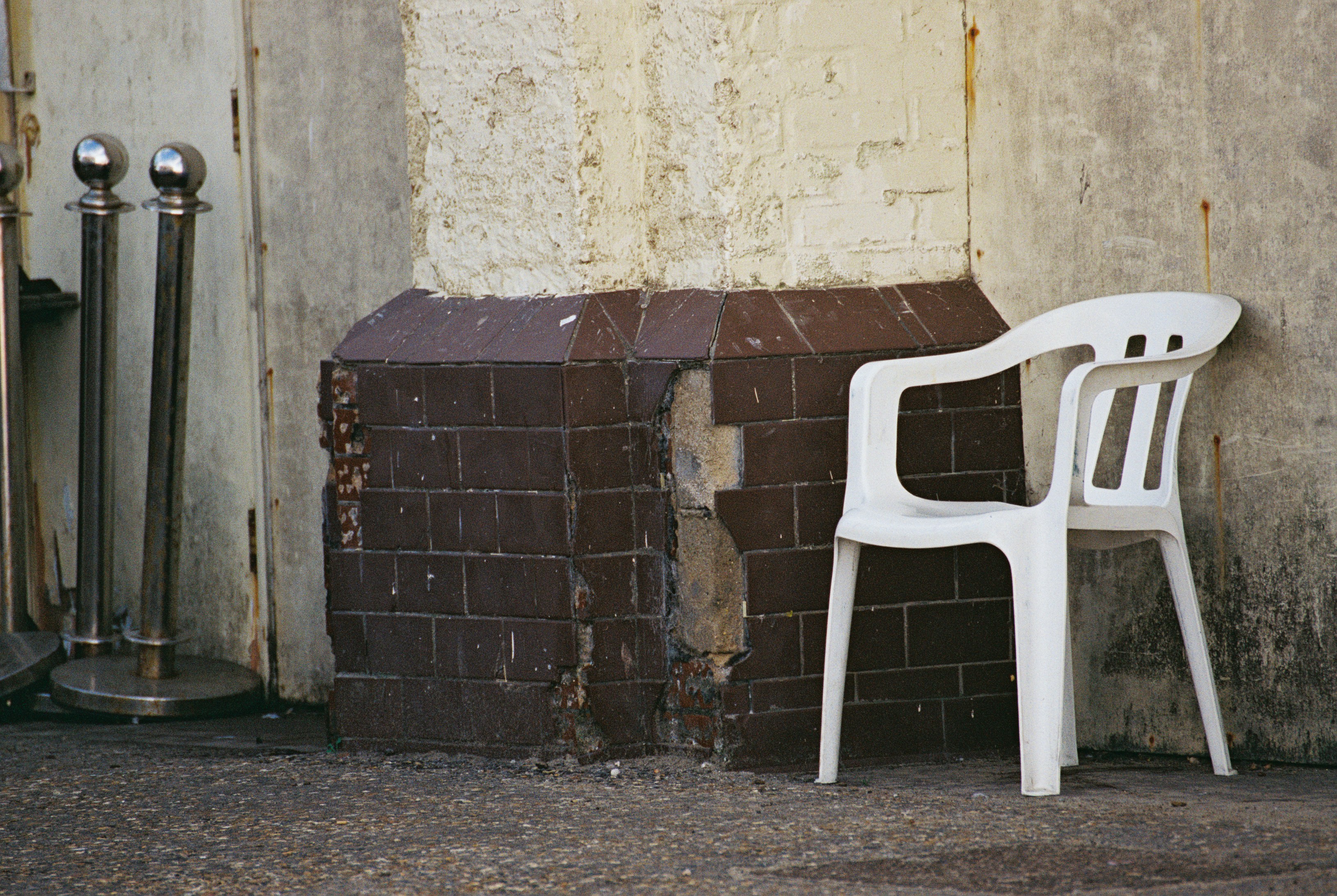 A white plastic chair beside a damaged brown tiled pillar on concrete