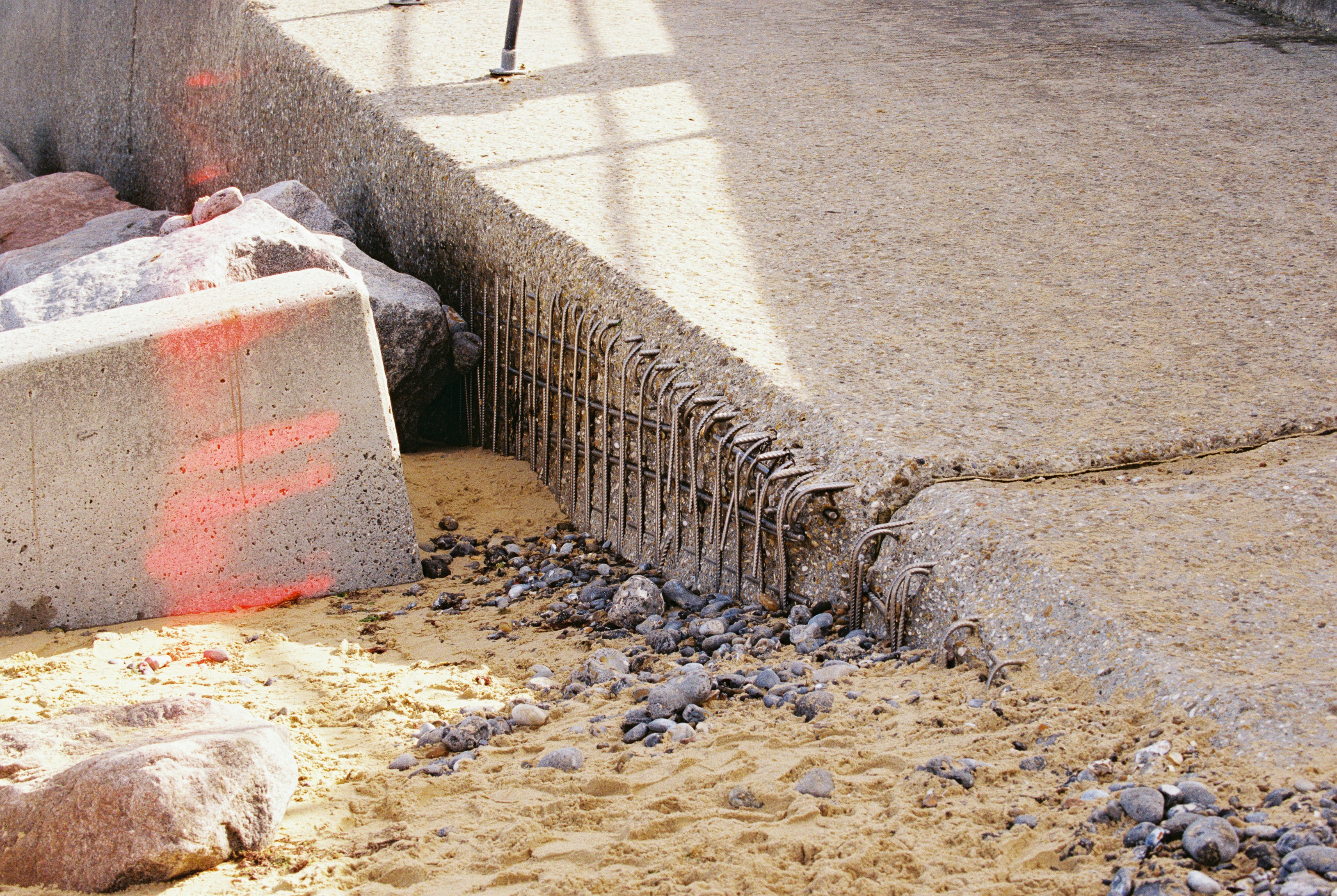 Cracked concrete slab with exposed steel rebar above sand and dark pebbles