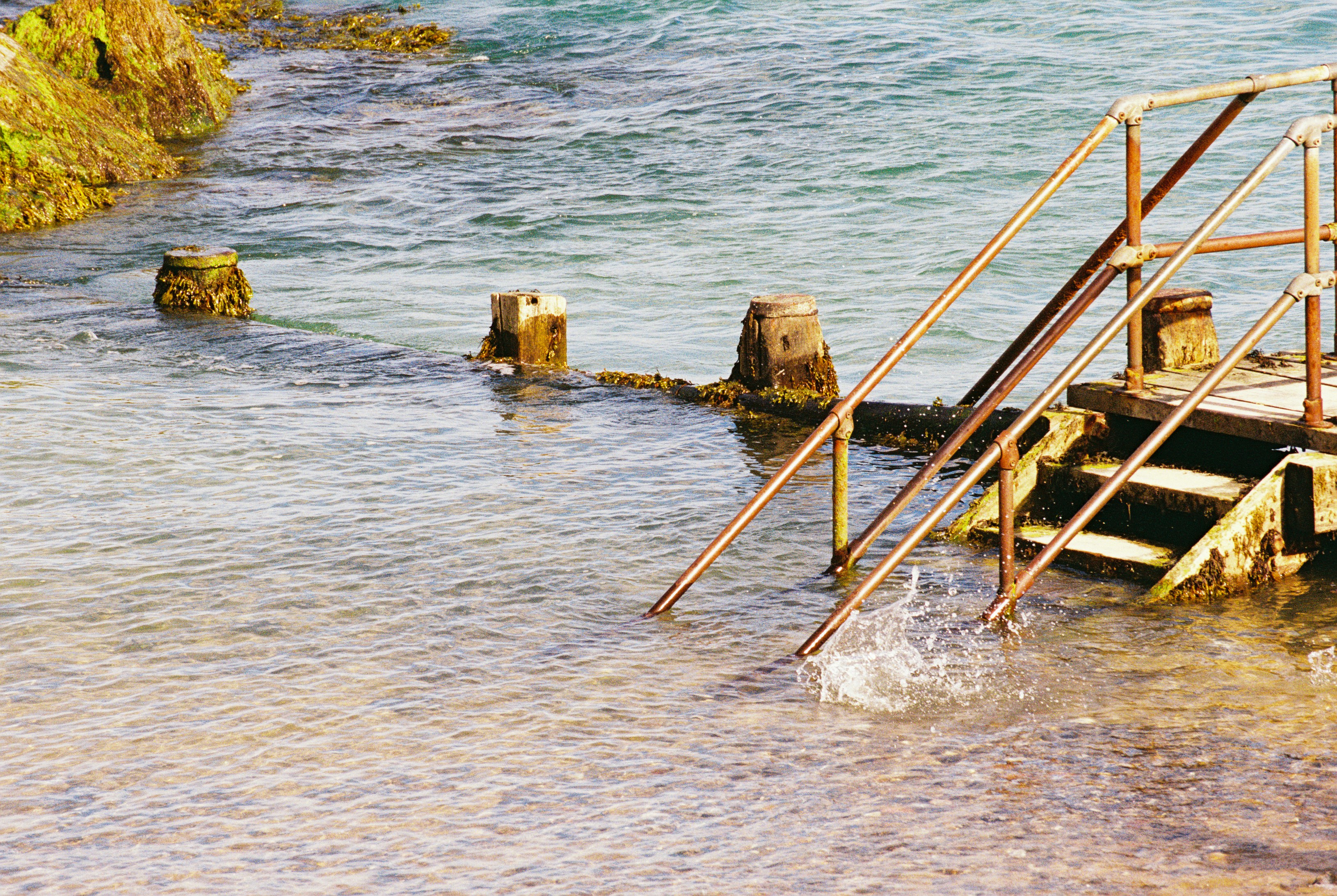 Timber steps with rusty handrails leading into shallow rippling sea water
