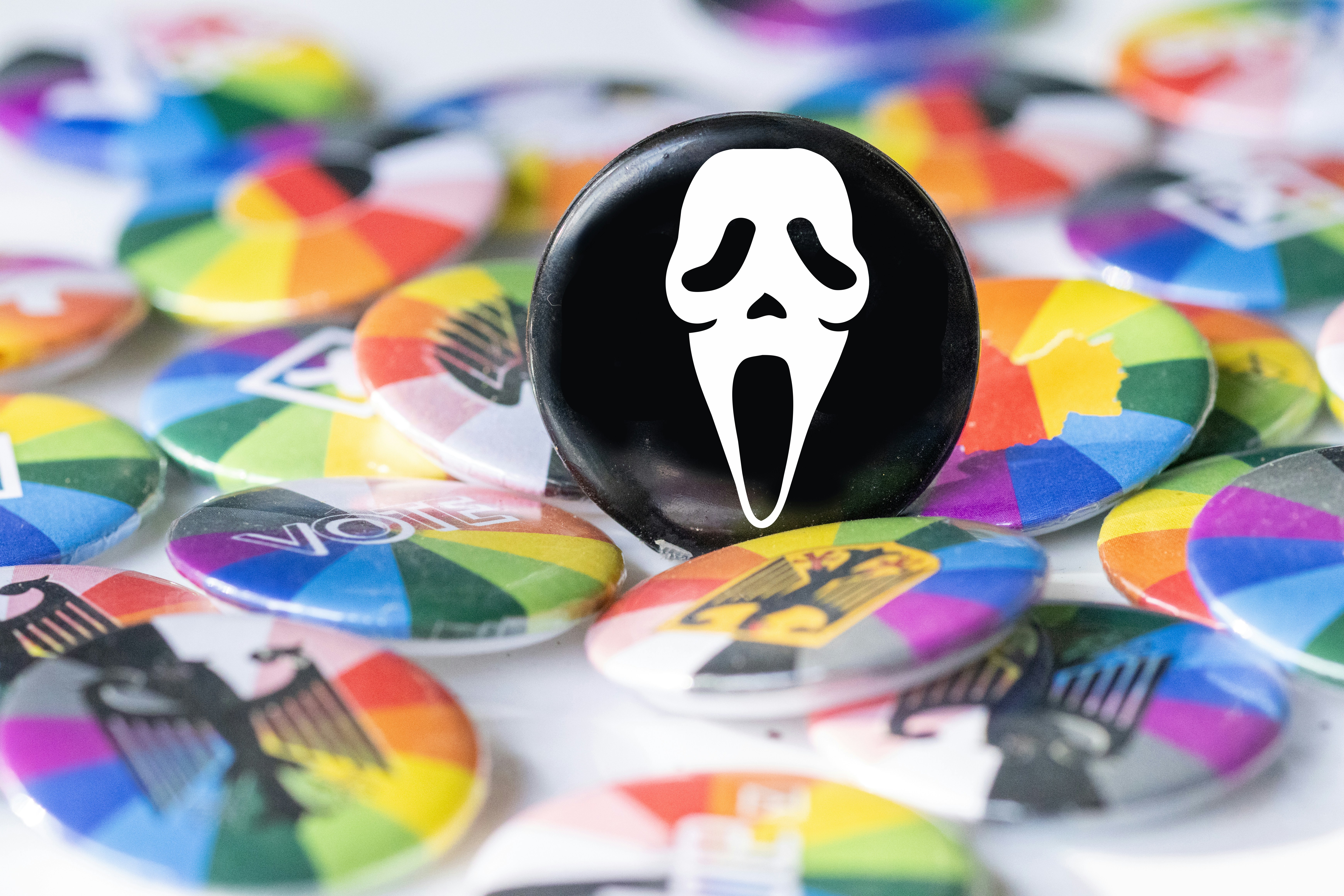 A black pin with a white Ghostface mask design resting on colorful circular badges