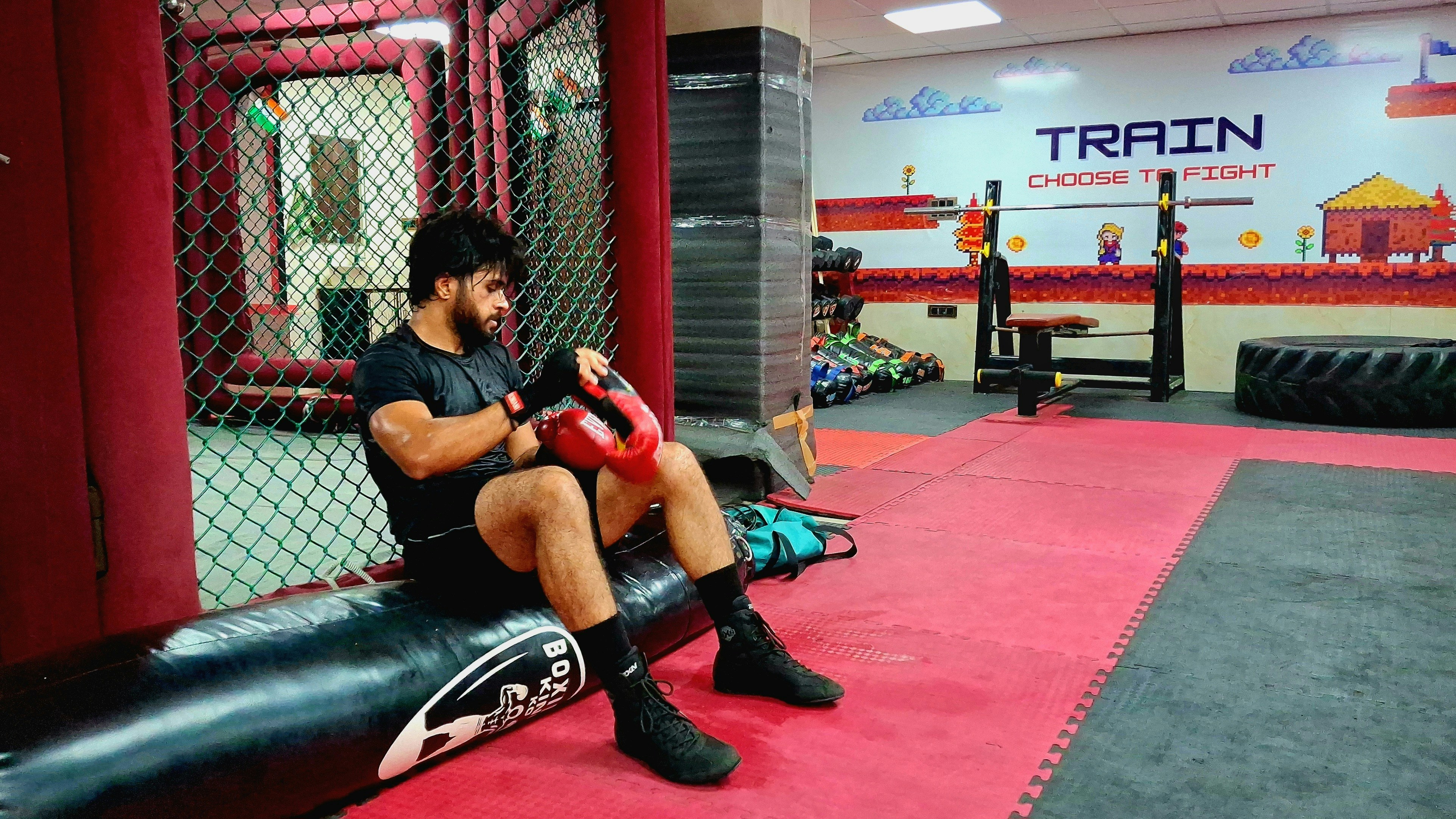 A man in a black t-shirt putting on red boxing gloves in a gym