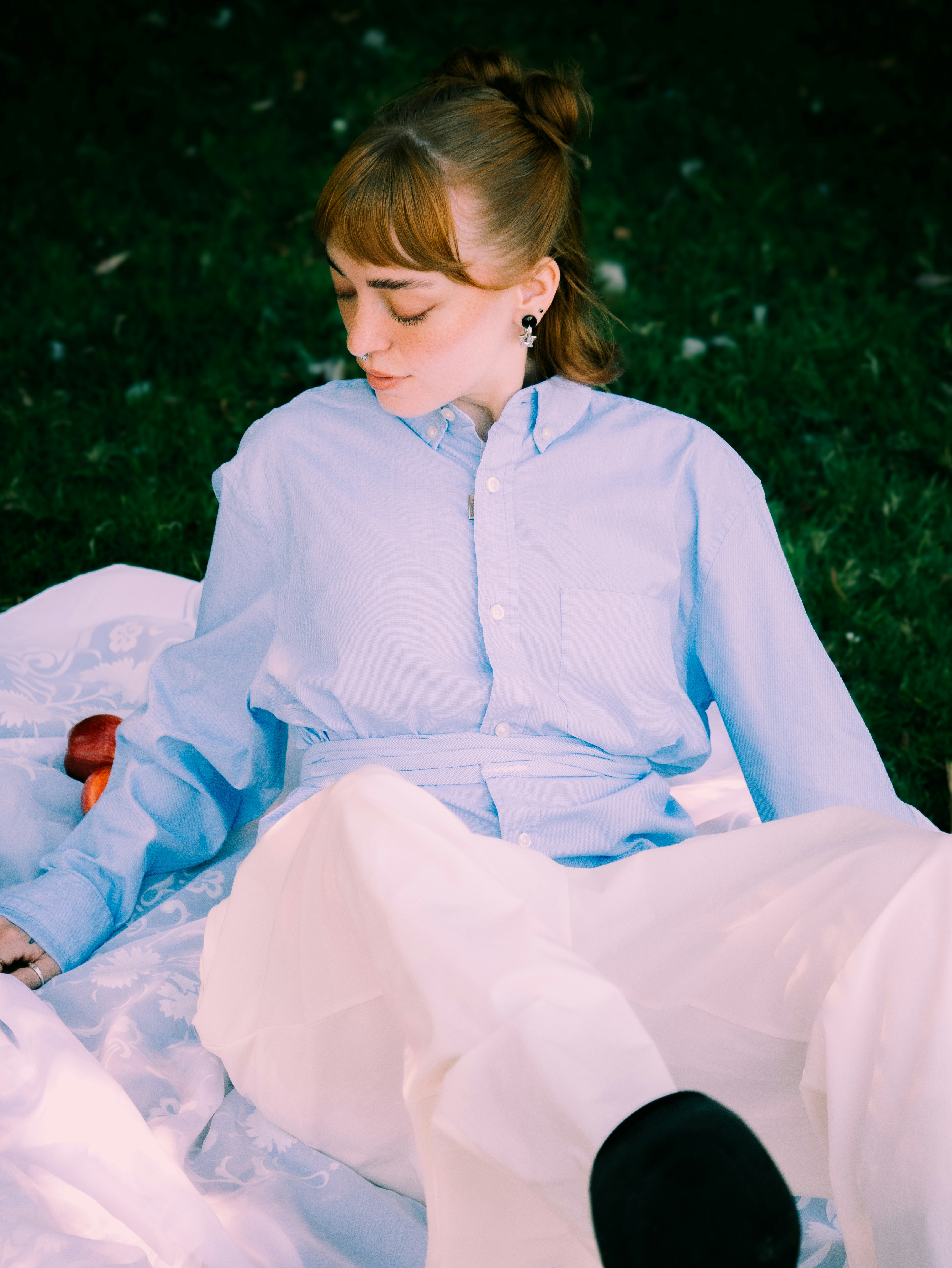 A woman in a light blue button-down shirt and white trousers sitting on a patterned blanket