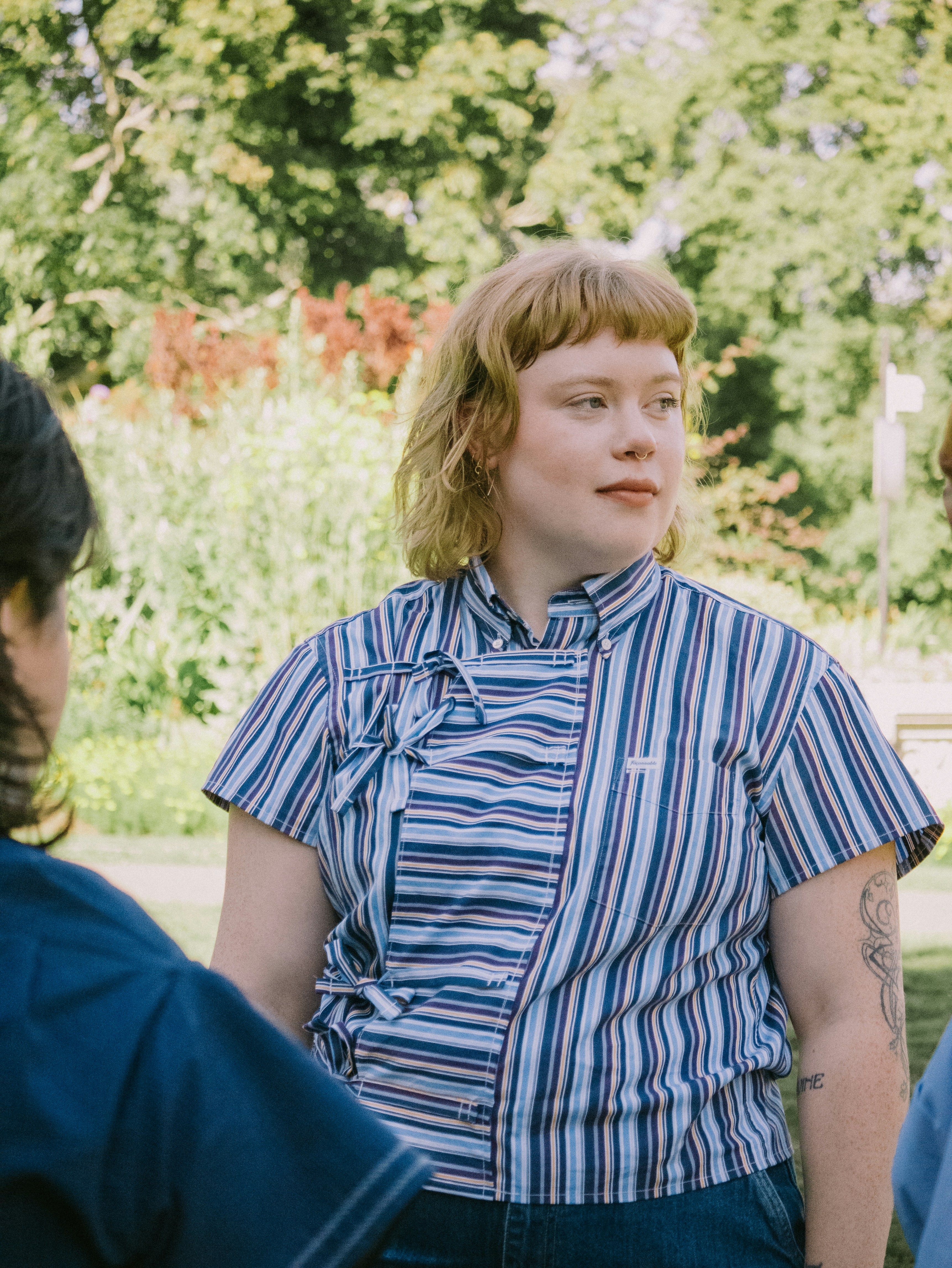 Uma mulher de cabelo loiro curto usando uma camisa listrada azul em um jardim