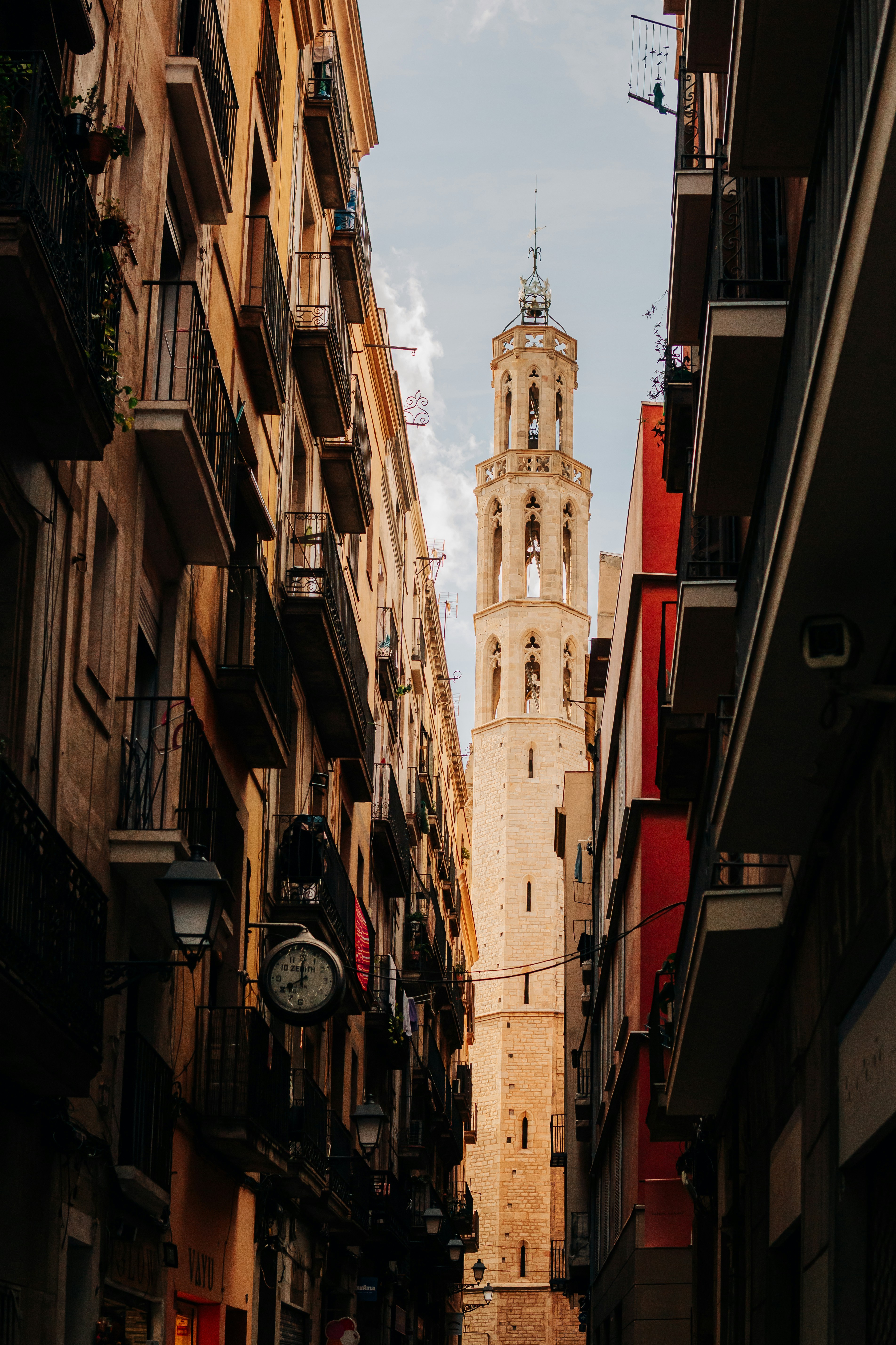 A tall stone bell tower framed by narrow apartment buildings along a street