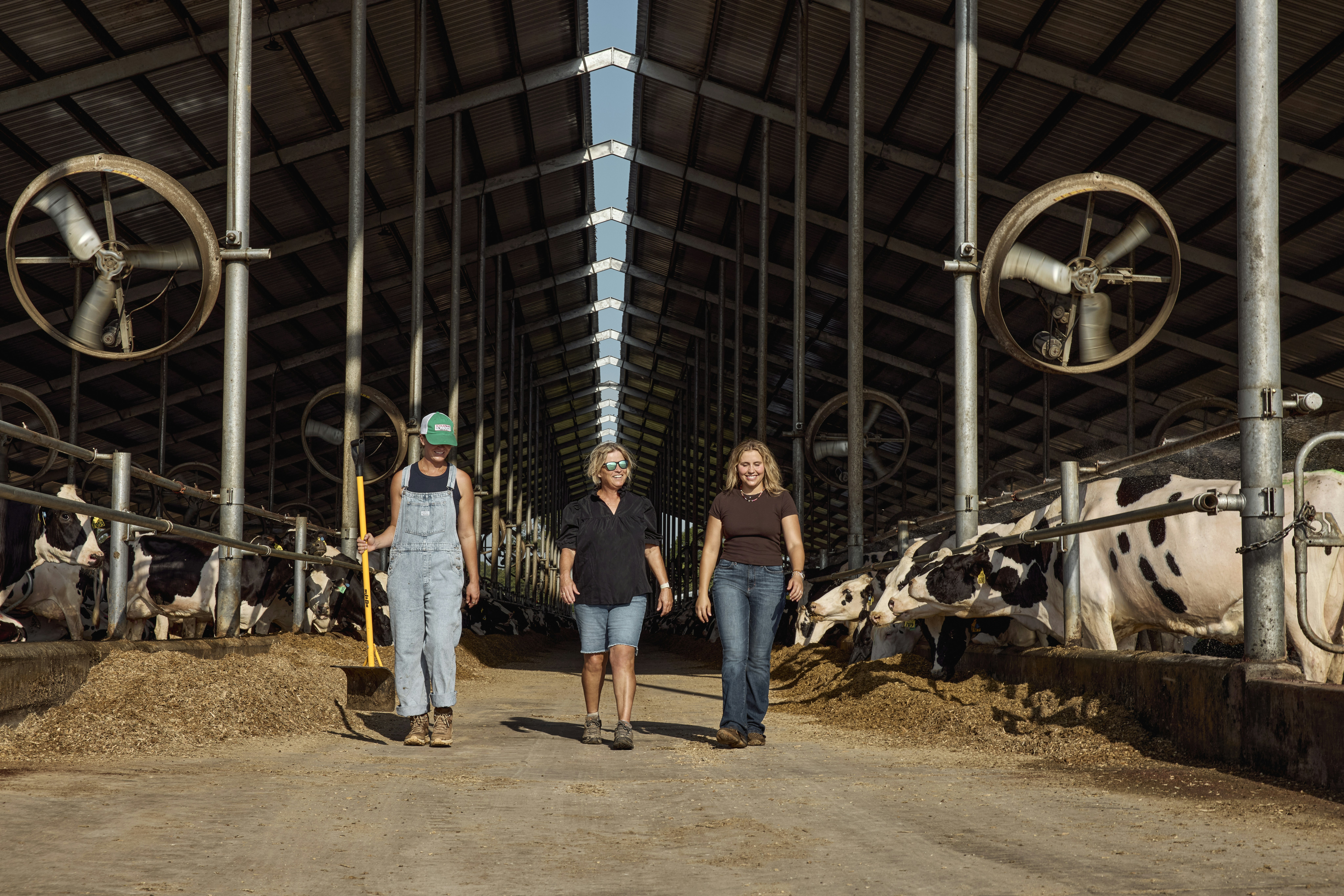 Three women walking through a dairy barn. Georgia, USA.