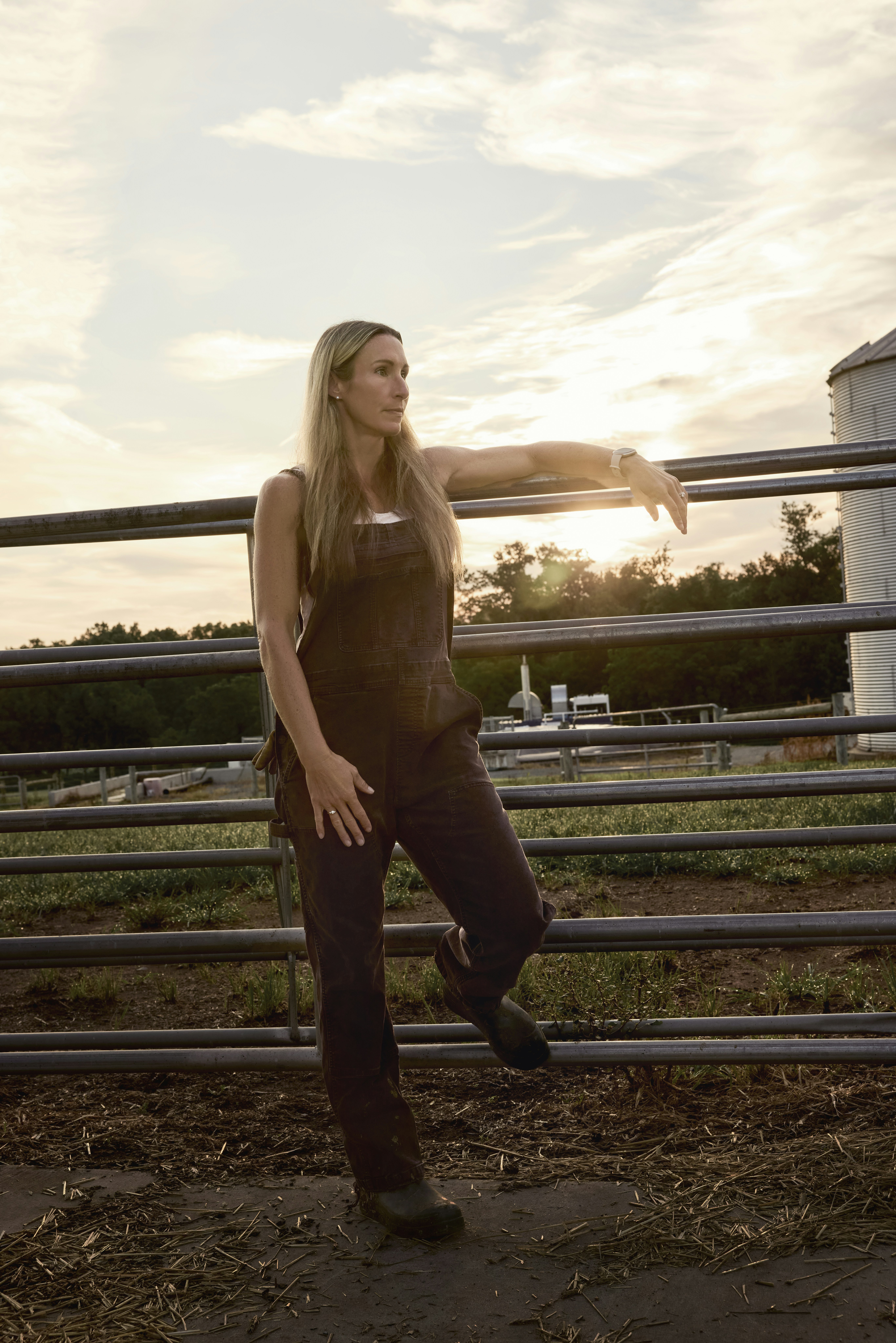 Woman leaning on a farm fence at sunrise. Maryland, USA.