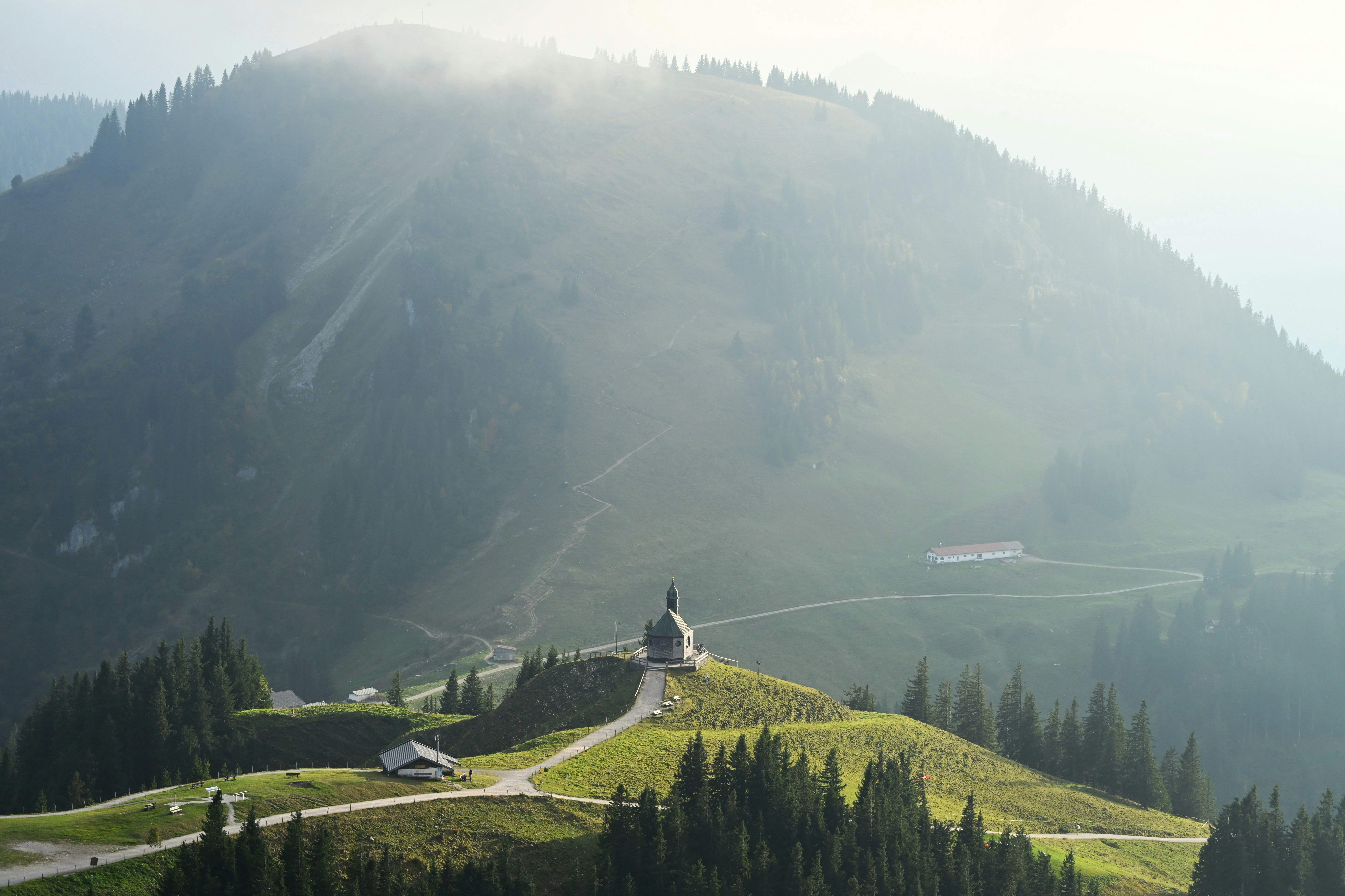 A small chapel on a grassy hill in the misty Bavarian Alps