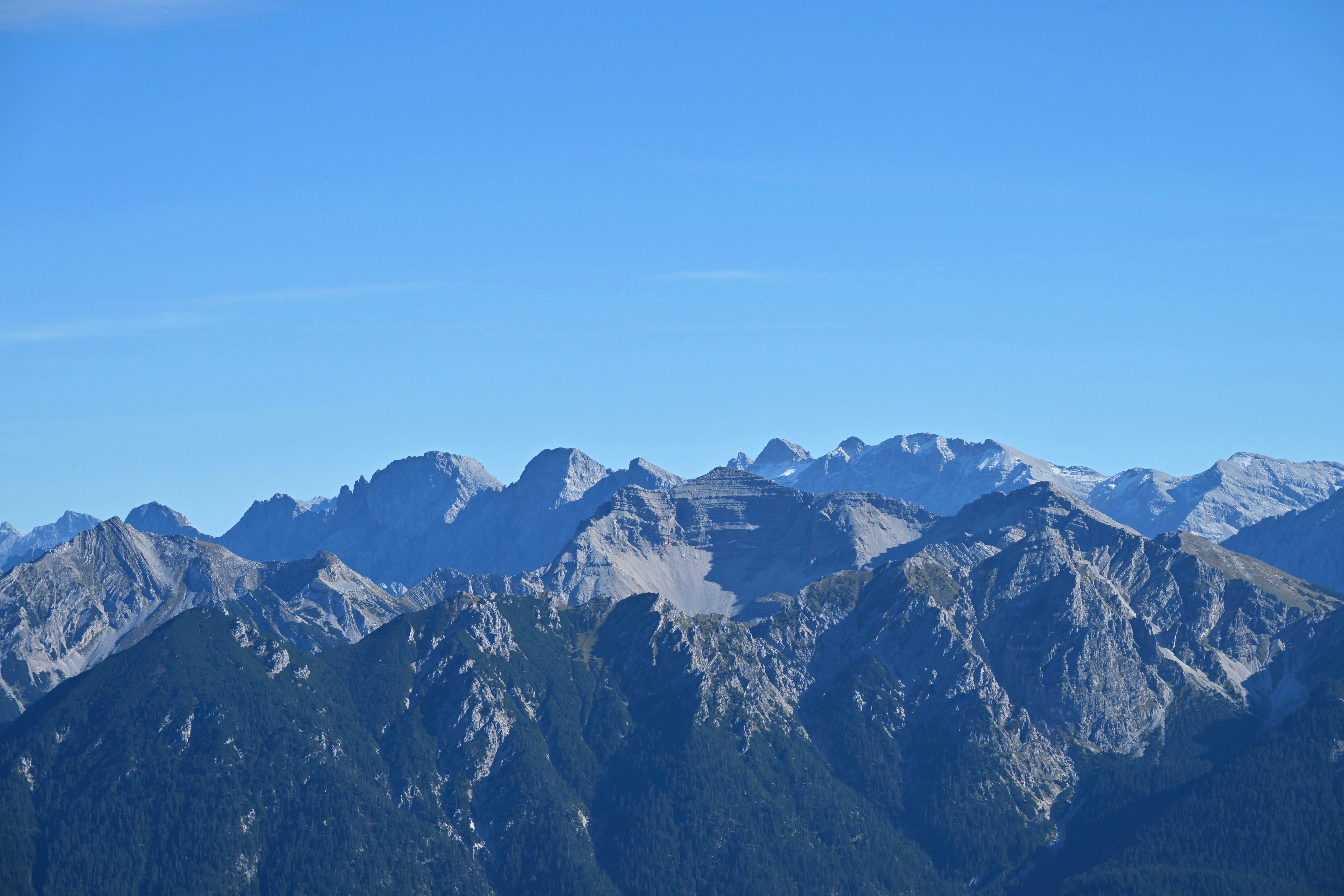 Jagged mountain peaks with rocky slopes and evergreen forests under a clear blue sky