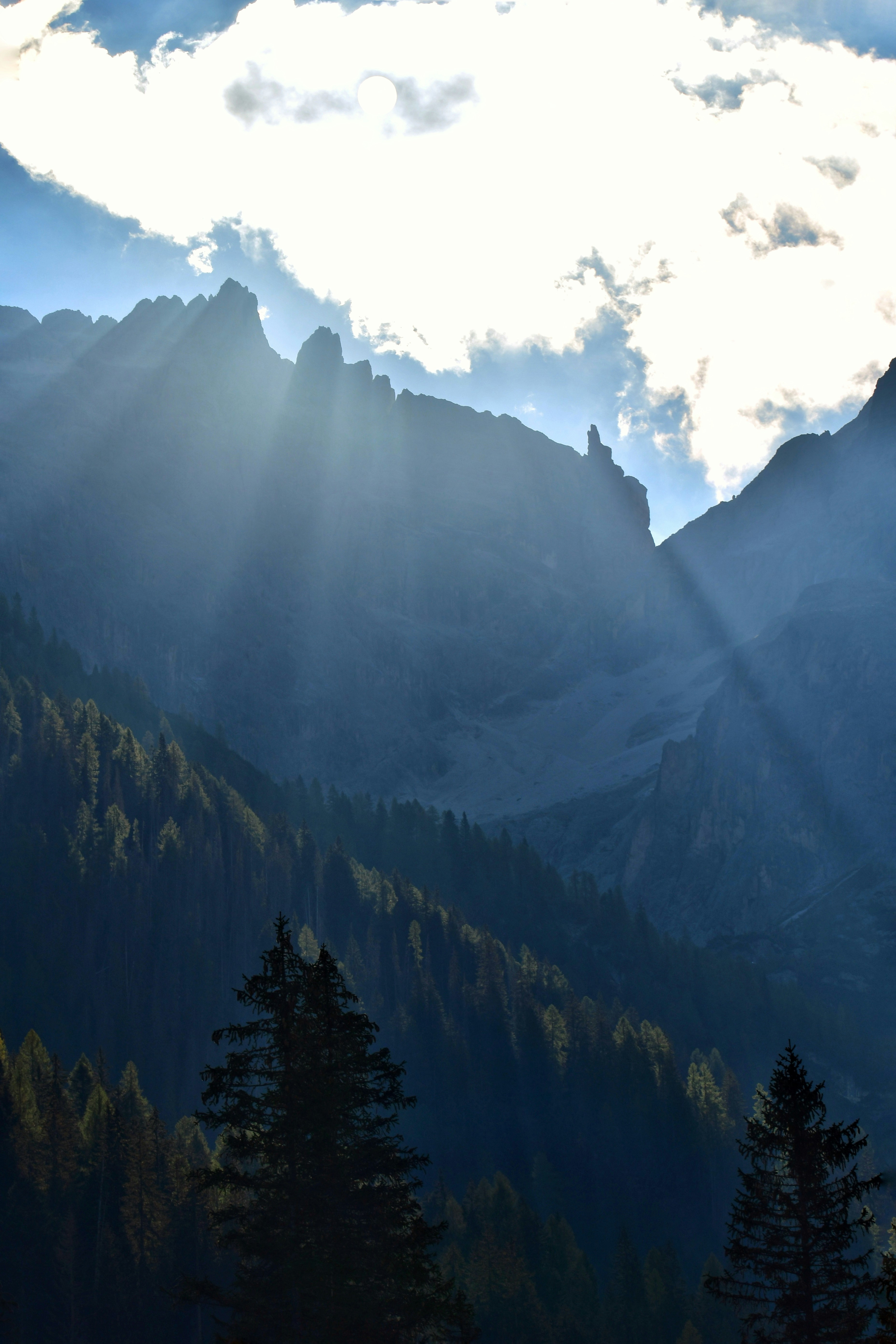 Sunlight streaming through clouds over a dark mountain range with pine trees