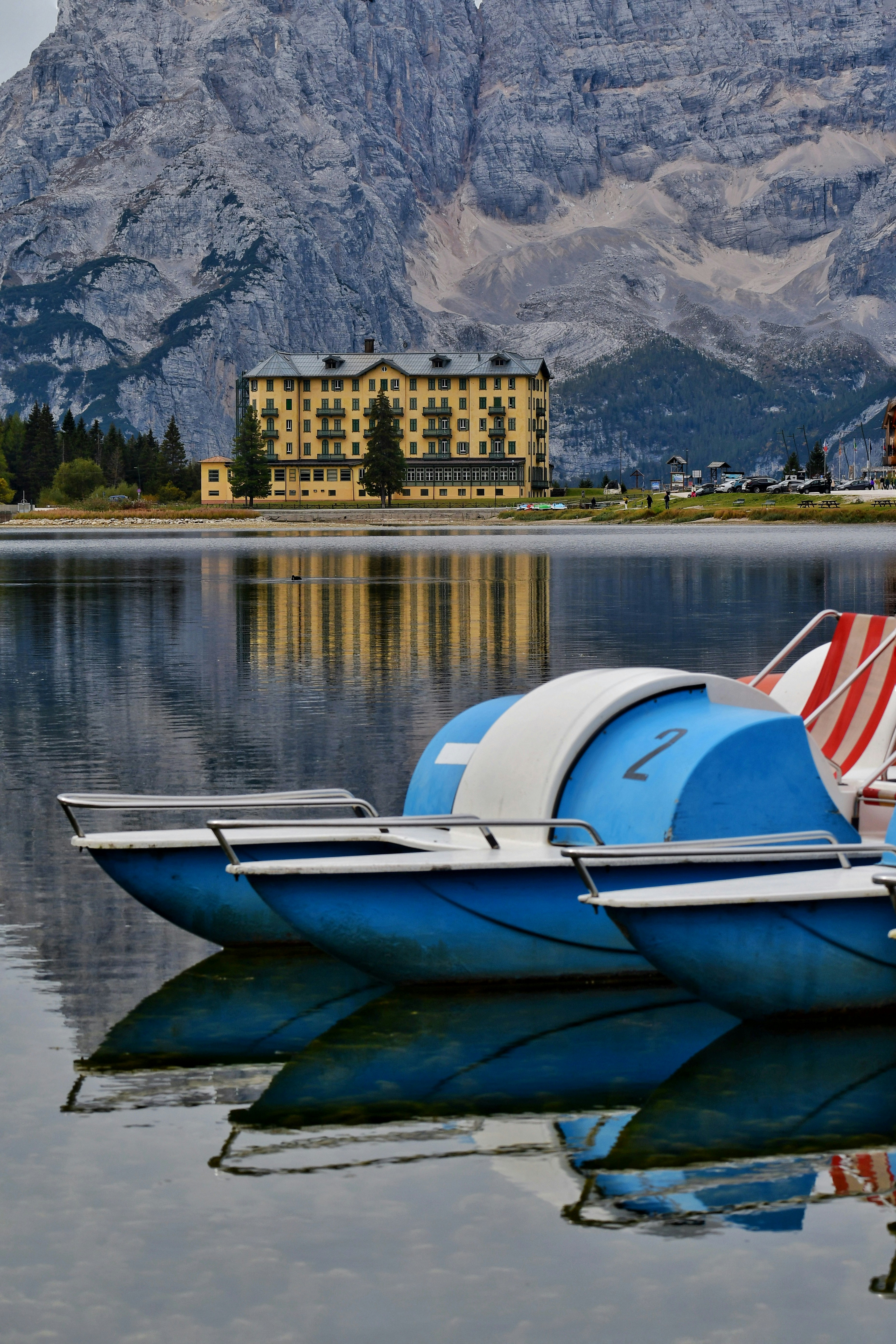 Blue pedal boats on a calm lake with a yellow hotel and mountains
