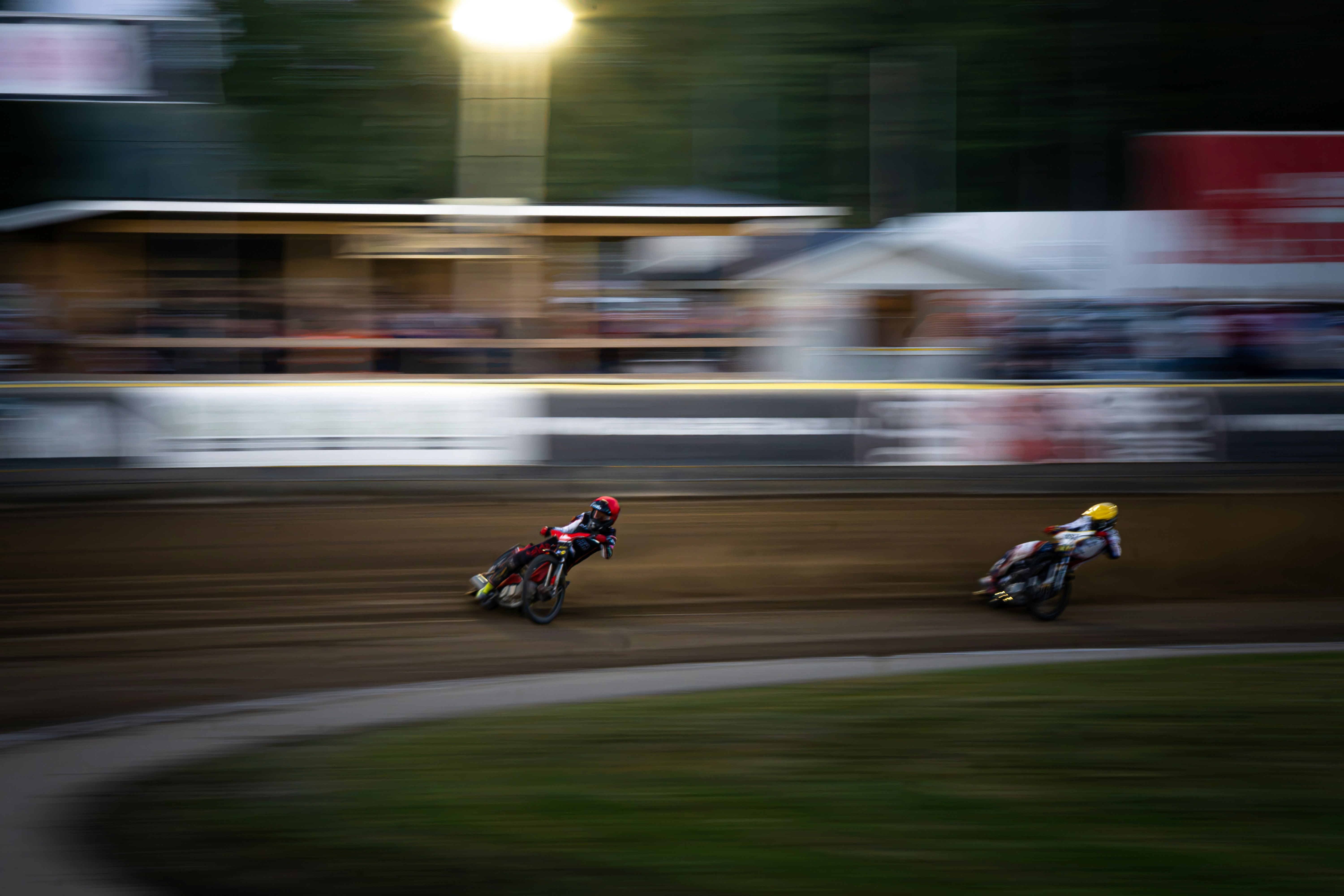 Two speedway motorcycle racers leaning into a turn on a dirt track with motion blur