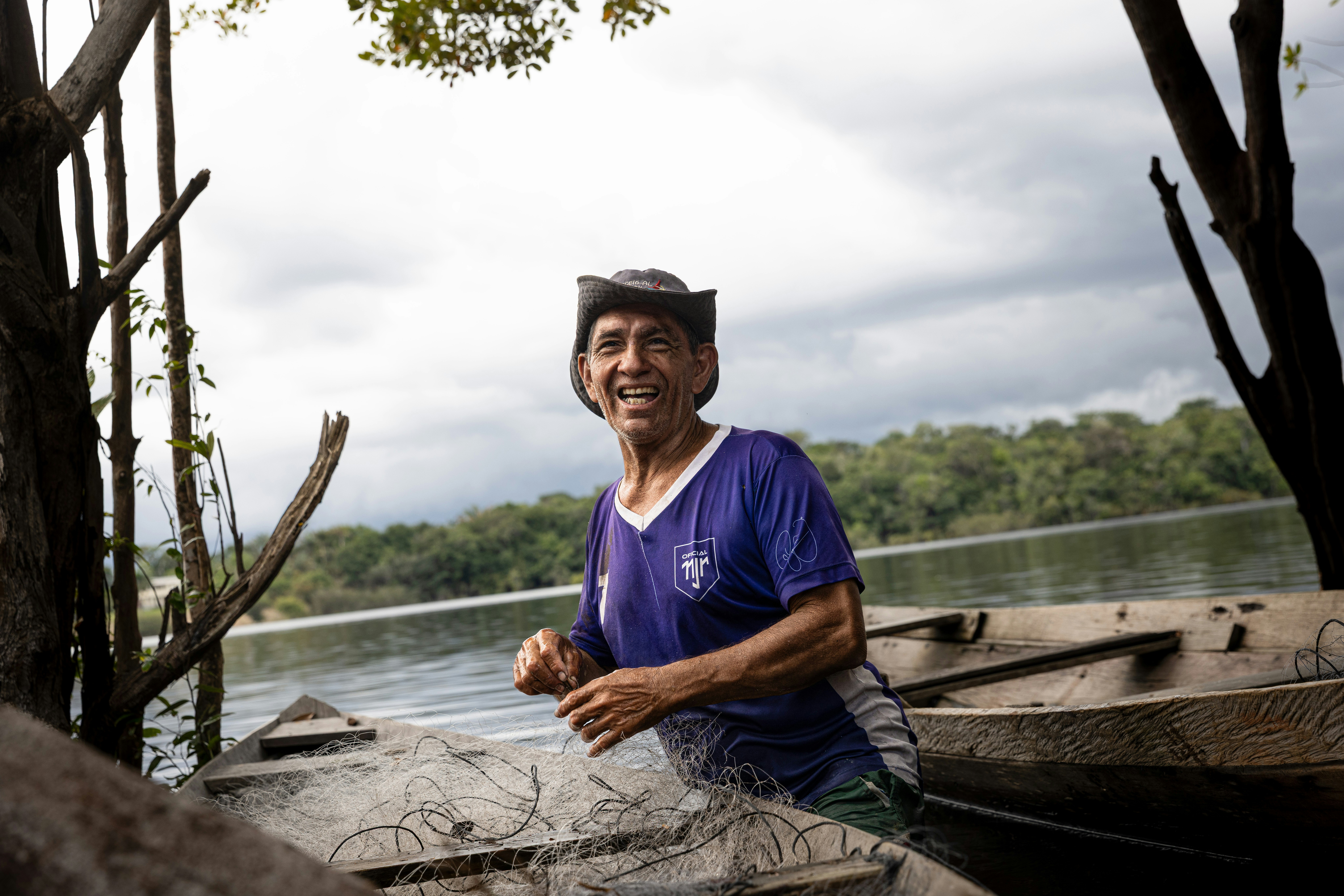 A smiling man in a hat and purple shirt mending a fishing net