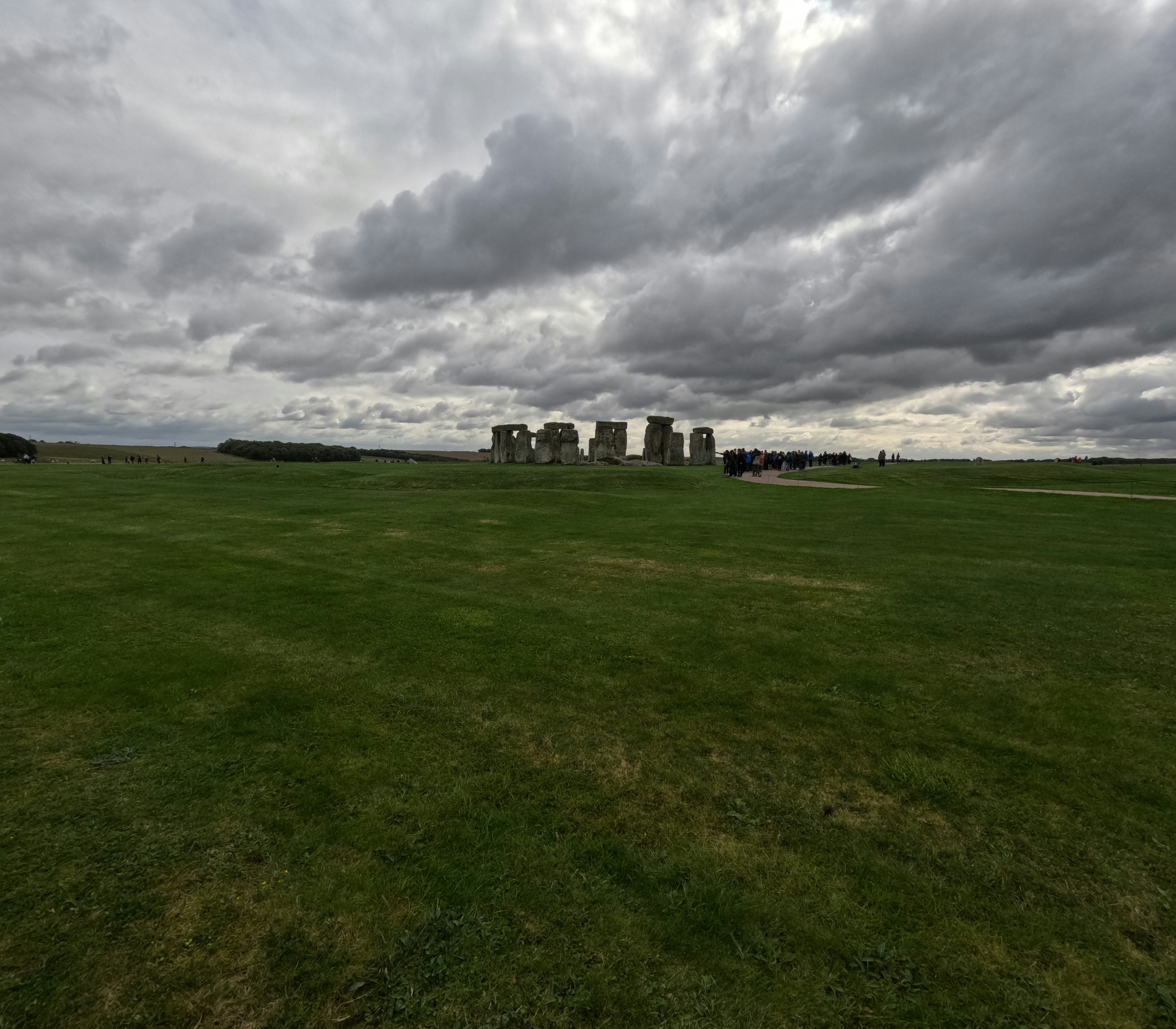 Stonehenge standing in a vast green field under a dramatic cloudy sky