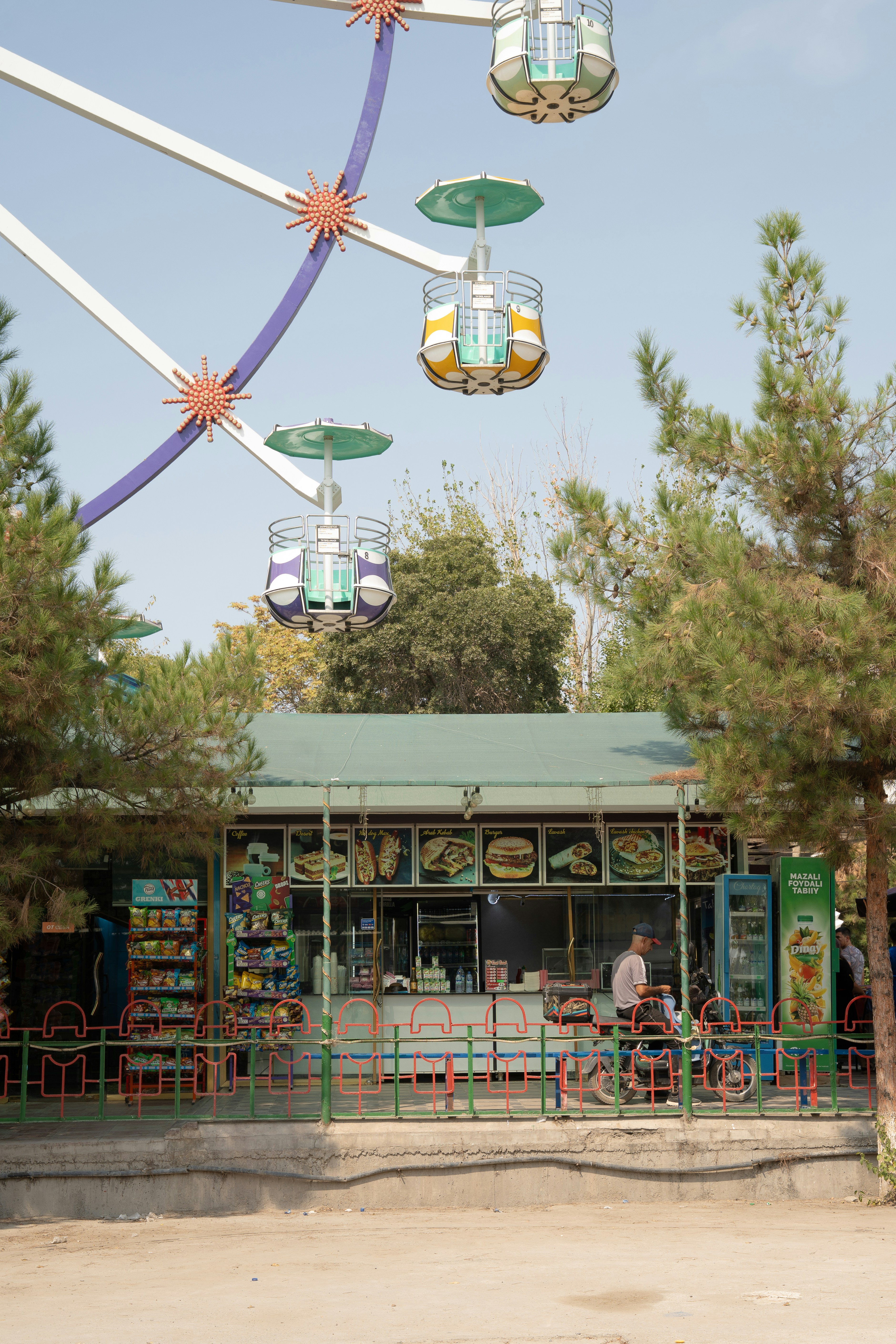 A food kiosk with a menu display beneath a ferris wheel in a park