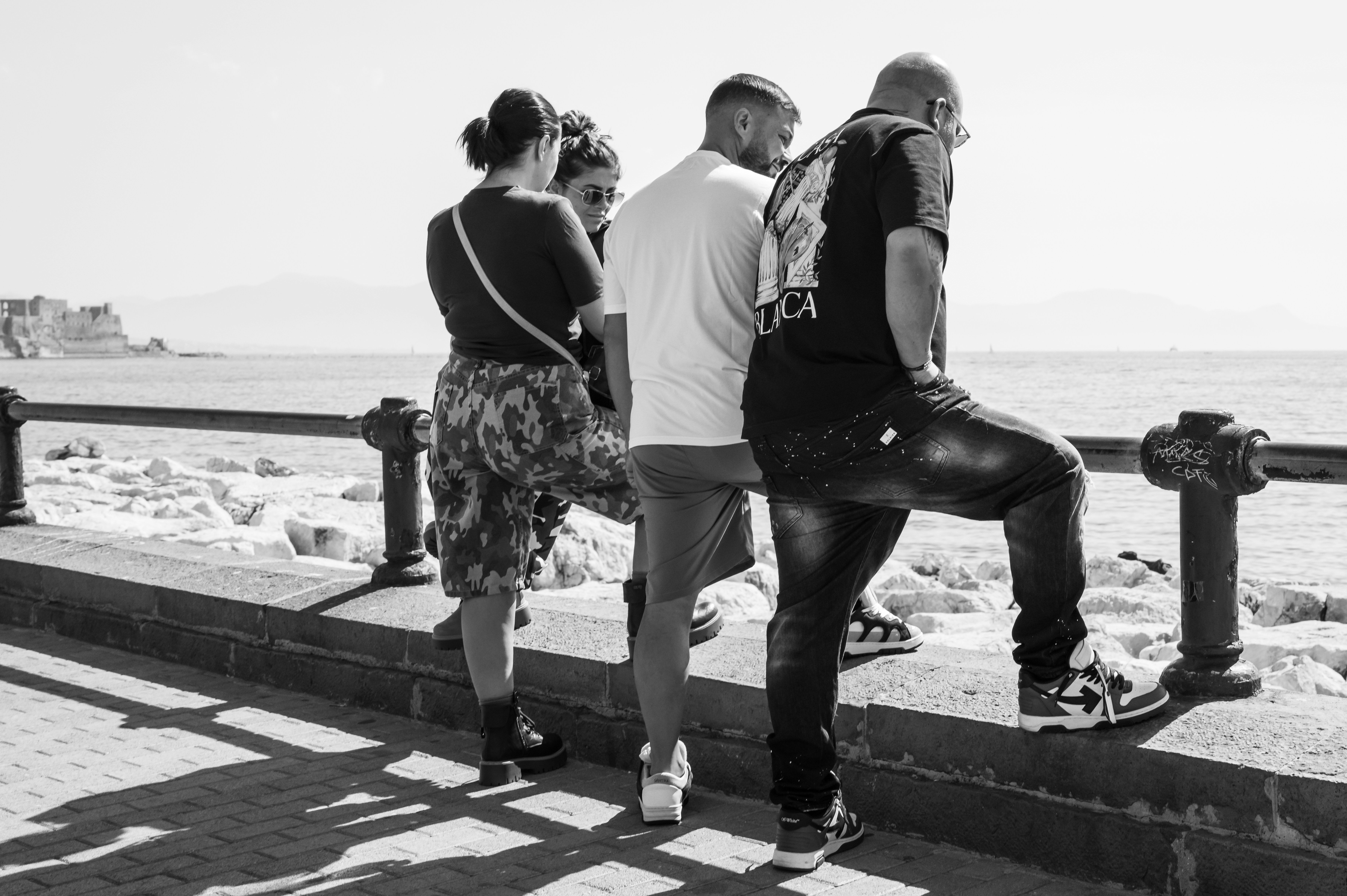 Four people leaning on a metal railing overlooking the sea on a sunny day