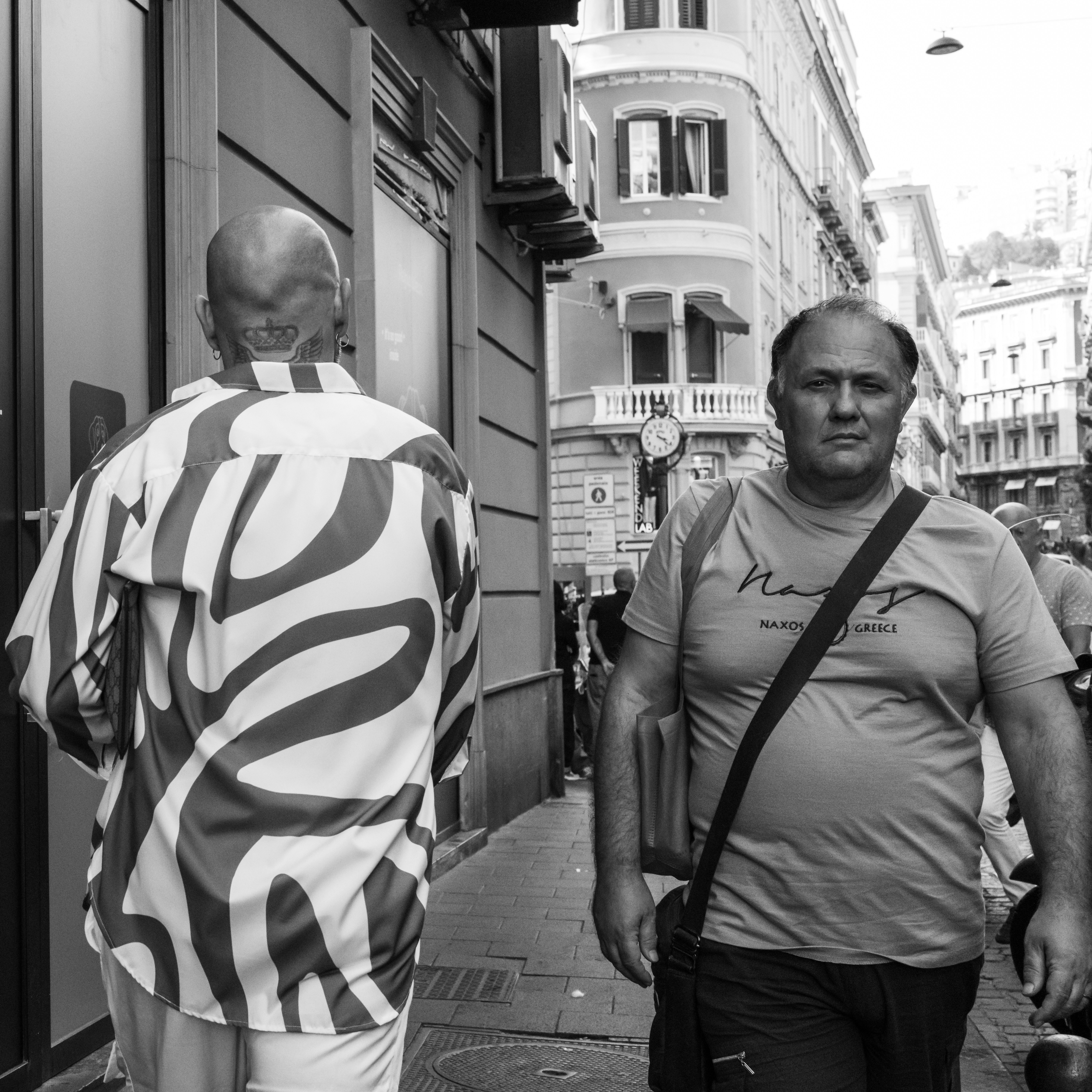 Two men walking on a city sidewalk past a building with ornate architecture