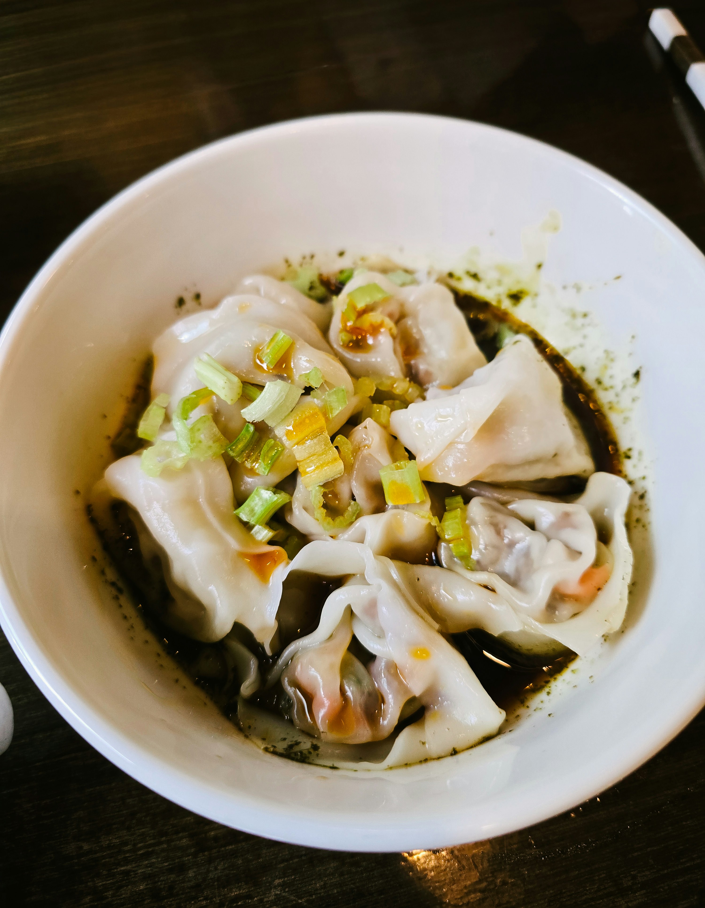 Wontons in a dark sauce with chili oil and chopped scallions in a bowl
