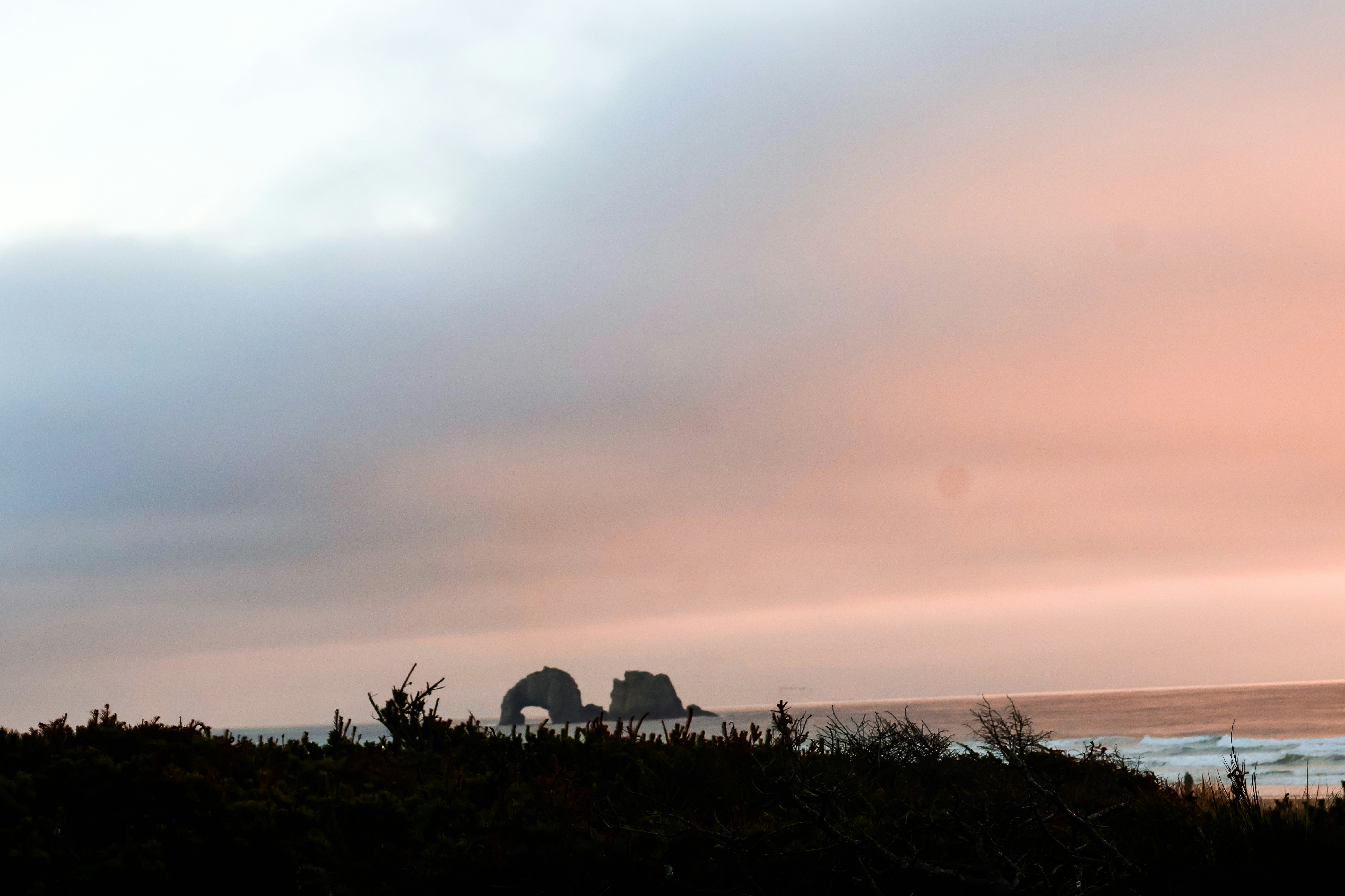 Sea stacks off the coast under a soft pink and grey sky at low sun