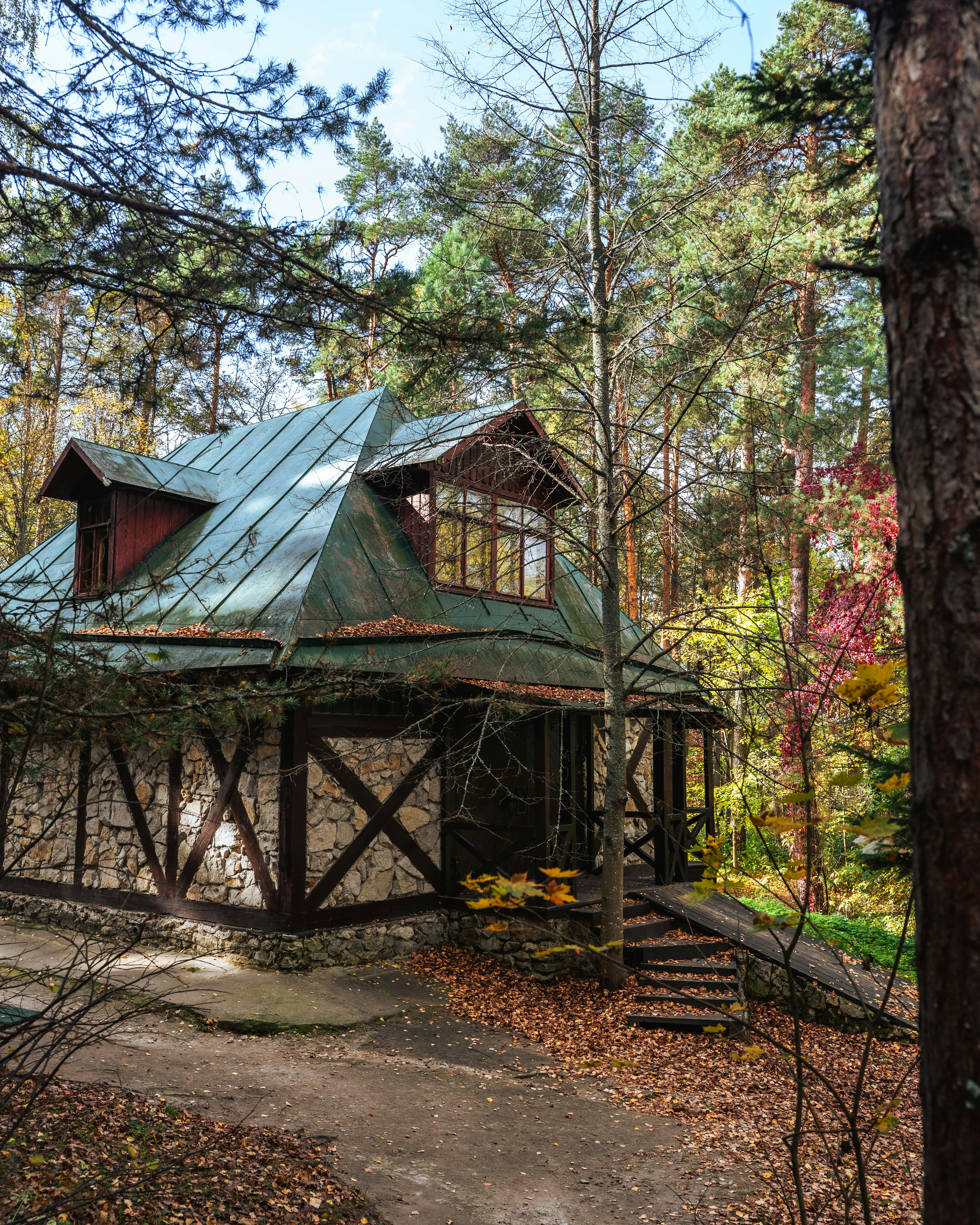 Un cottage en pierre au toit métallique vert niché dans une forêt d’automne dense