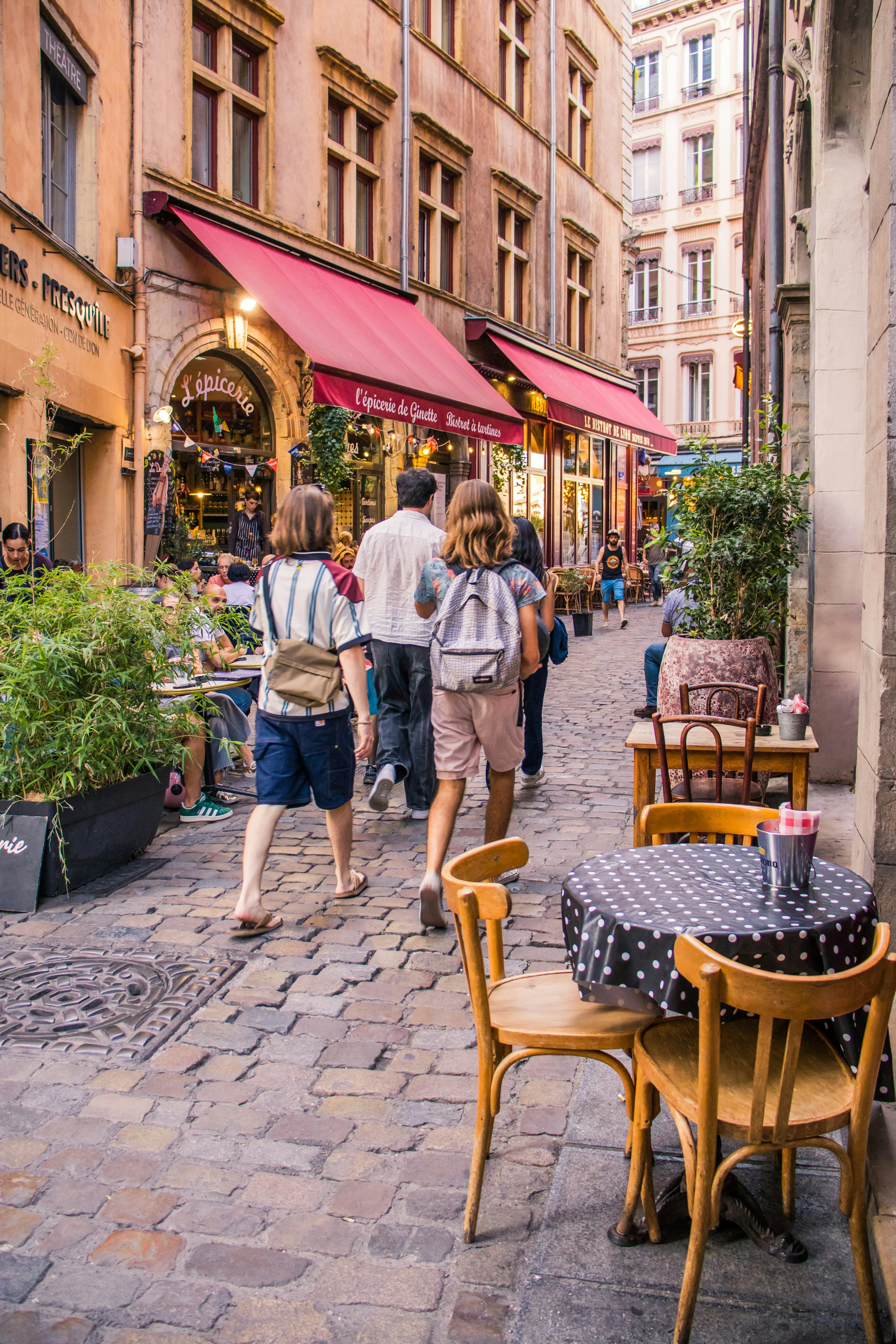 Pessoas caminhando por uma rua de paralelepípedos ladeada por mesas de café ao ar livre em Lyon