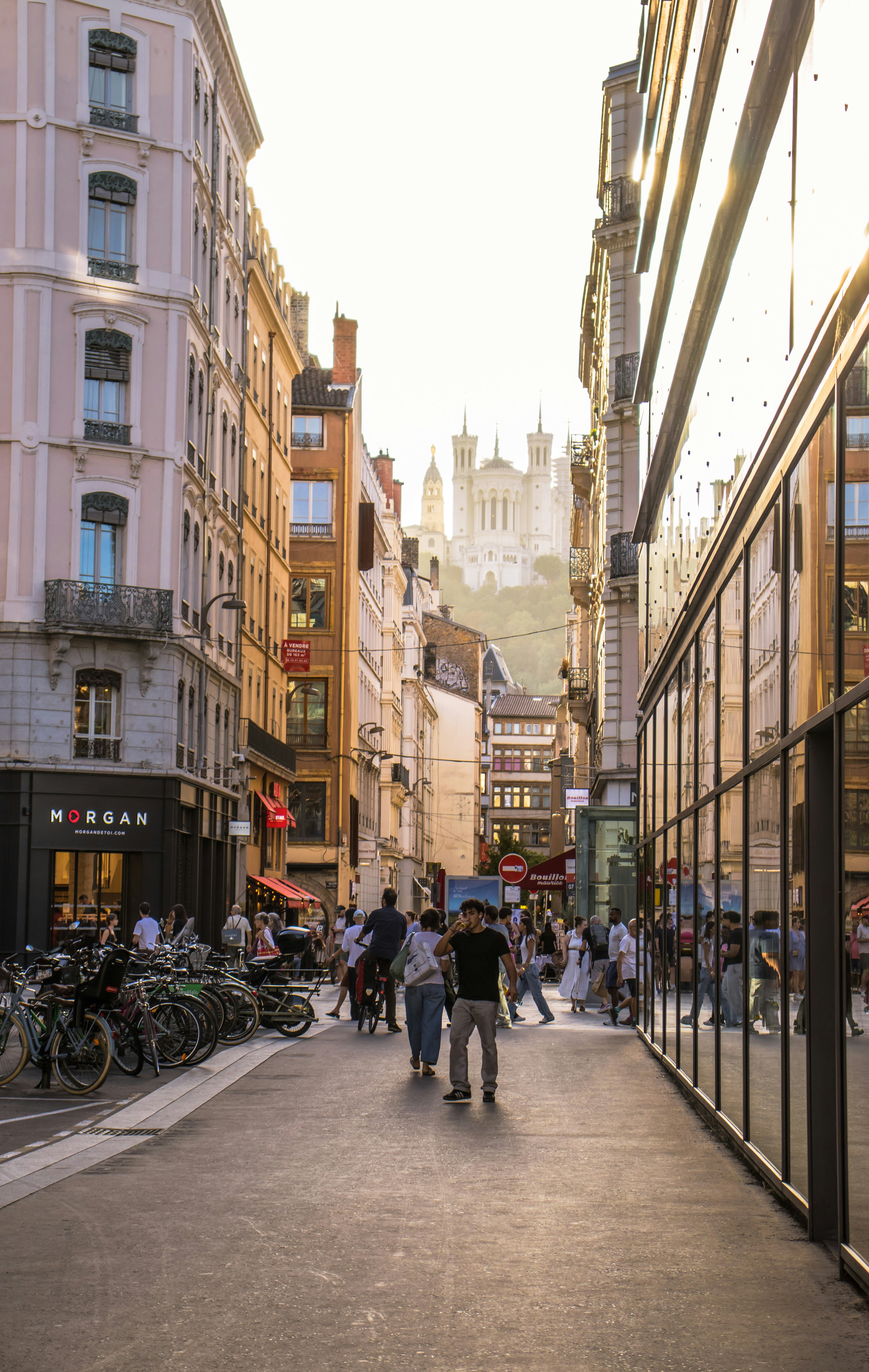 Pessoas caminhando por uma rua em Lyon com a Basílica de Notre-Dame de Fourvière