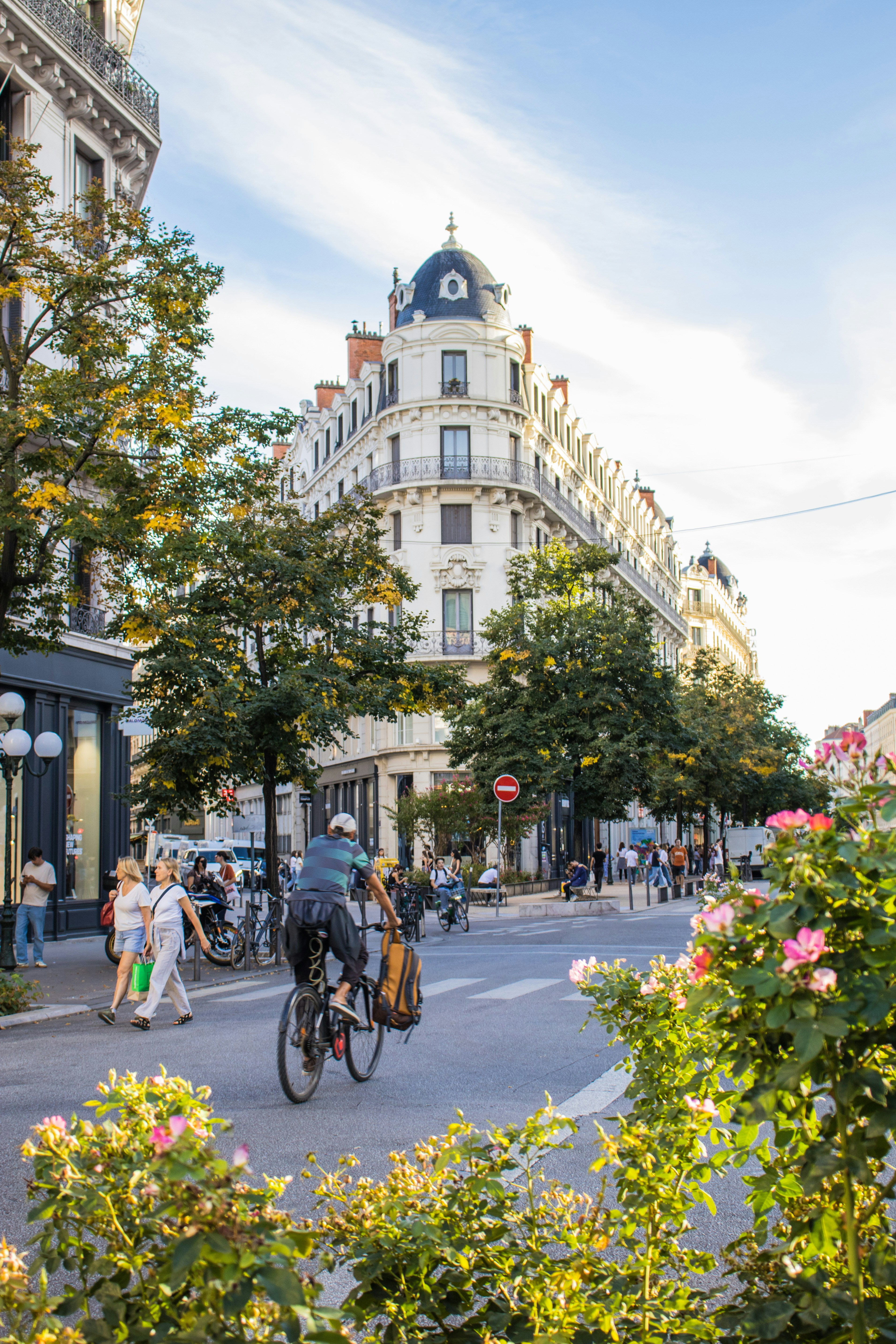 Um ciclista pedalando por uma rua movimentada em Lyon com prédios históricos e árvores