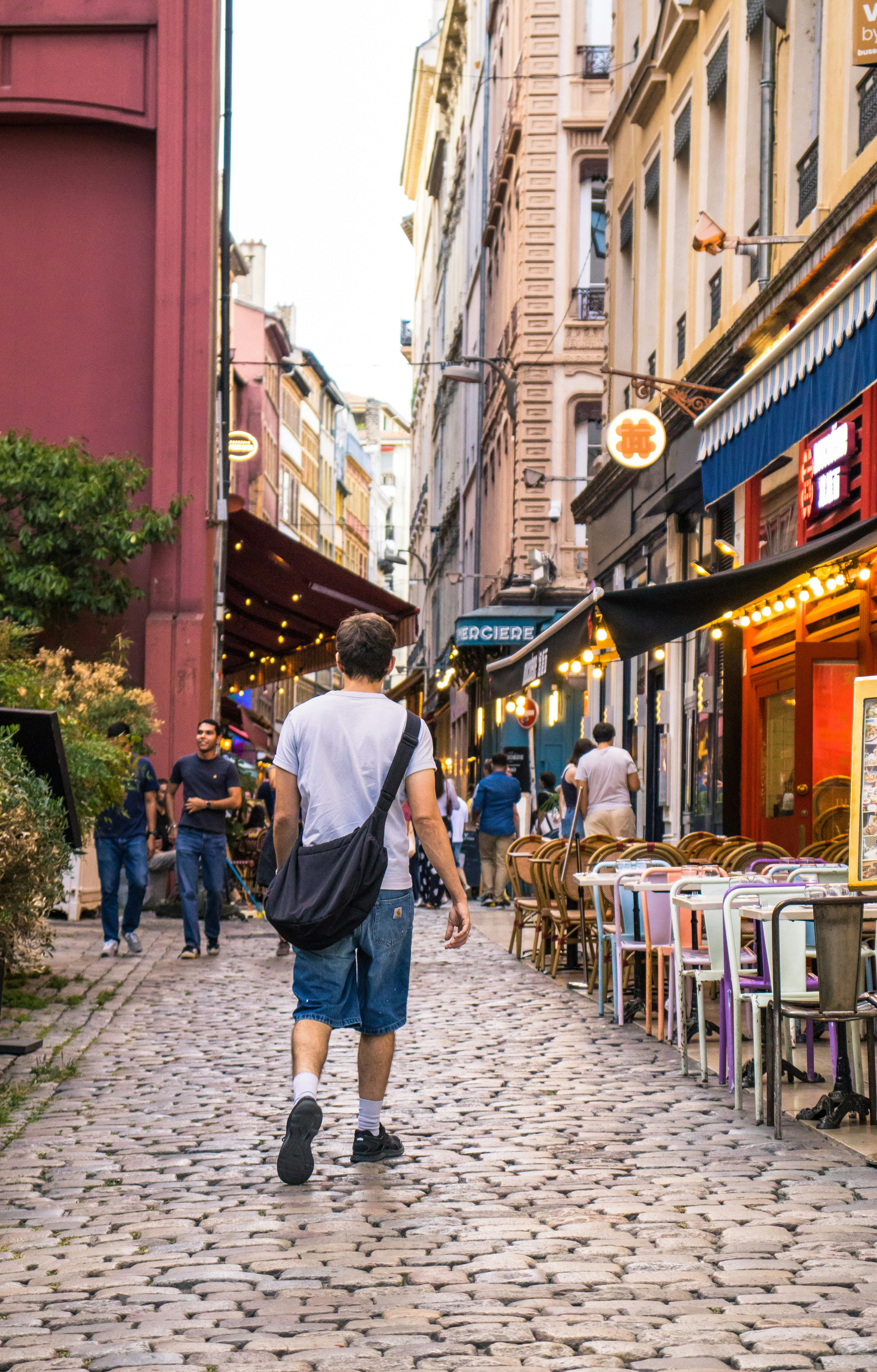 Uma pessoa caminhando por uma rua de paralelepípedos ladeada por mesas de restaurante ao ar livre