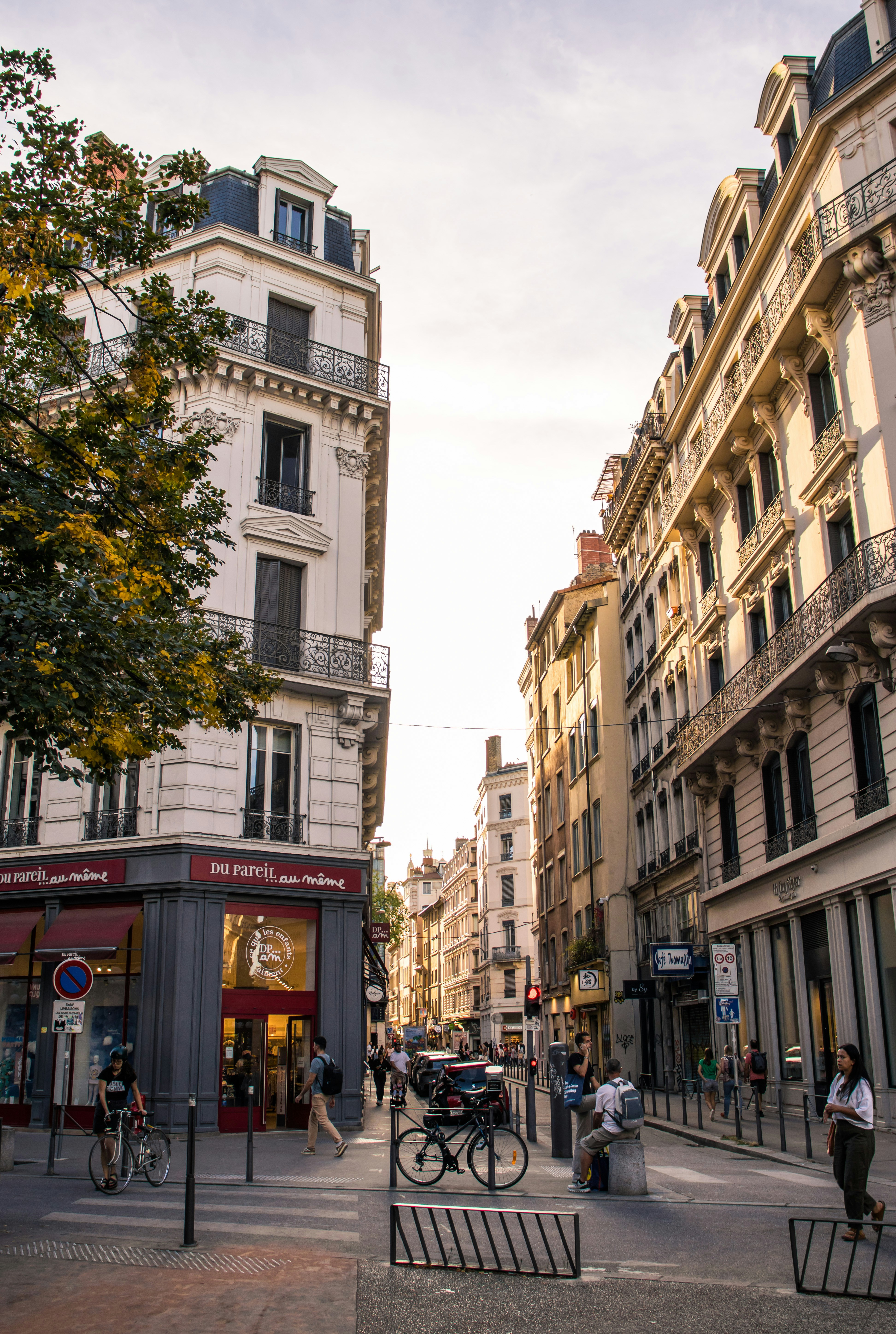 Pessoas caminhando e pedalando em uma rua ladeada por altos prédios históricos em Lyon