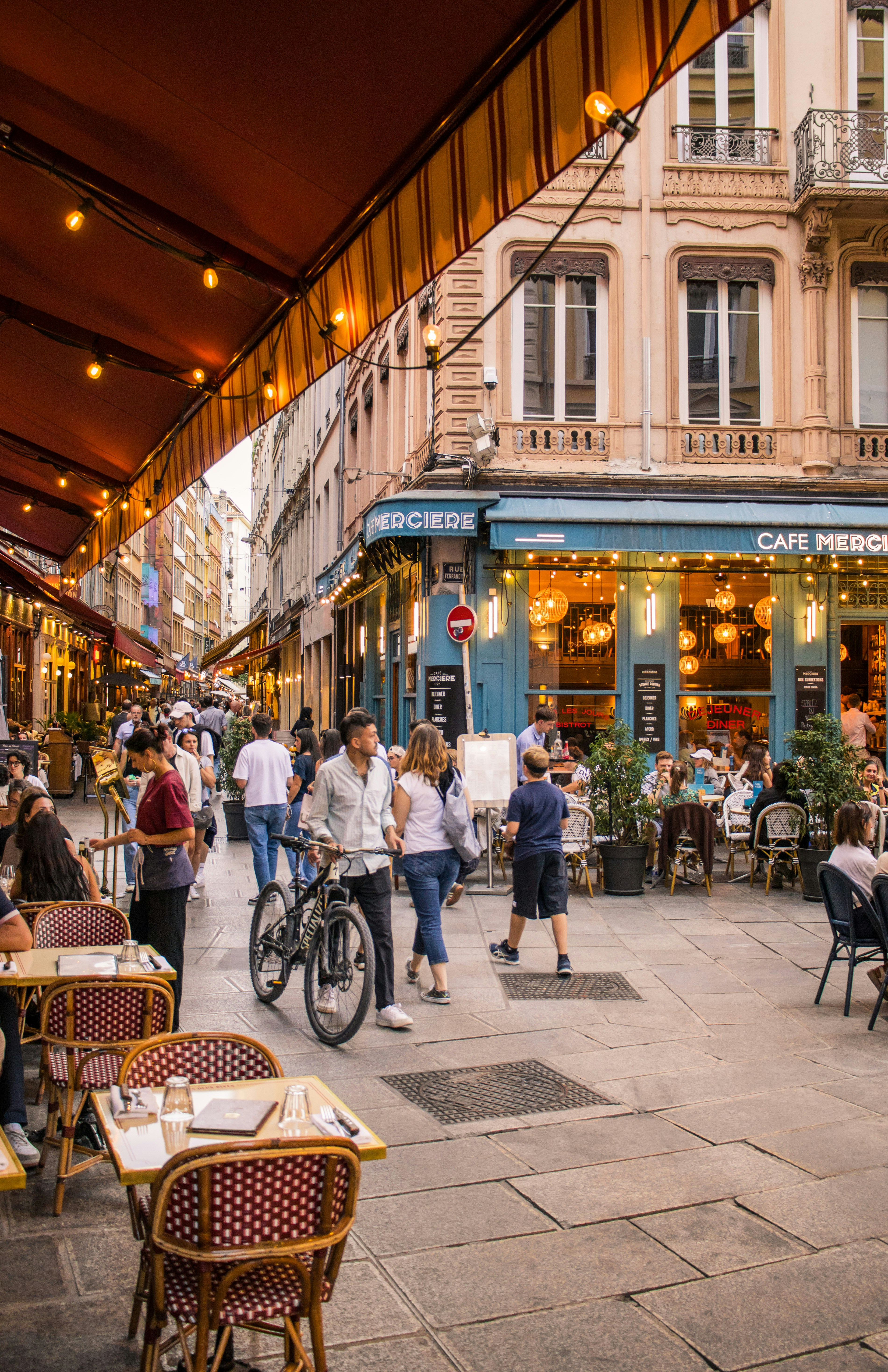 Pessoas caminhando por uma rua de pedestres em Lyon passando por um café com assentos ao ar livre