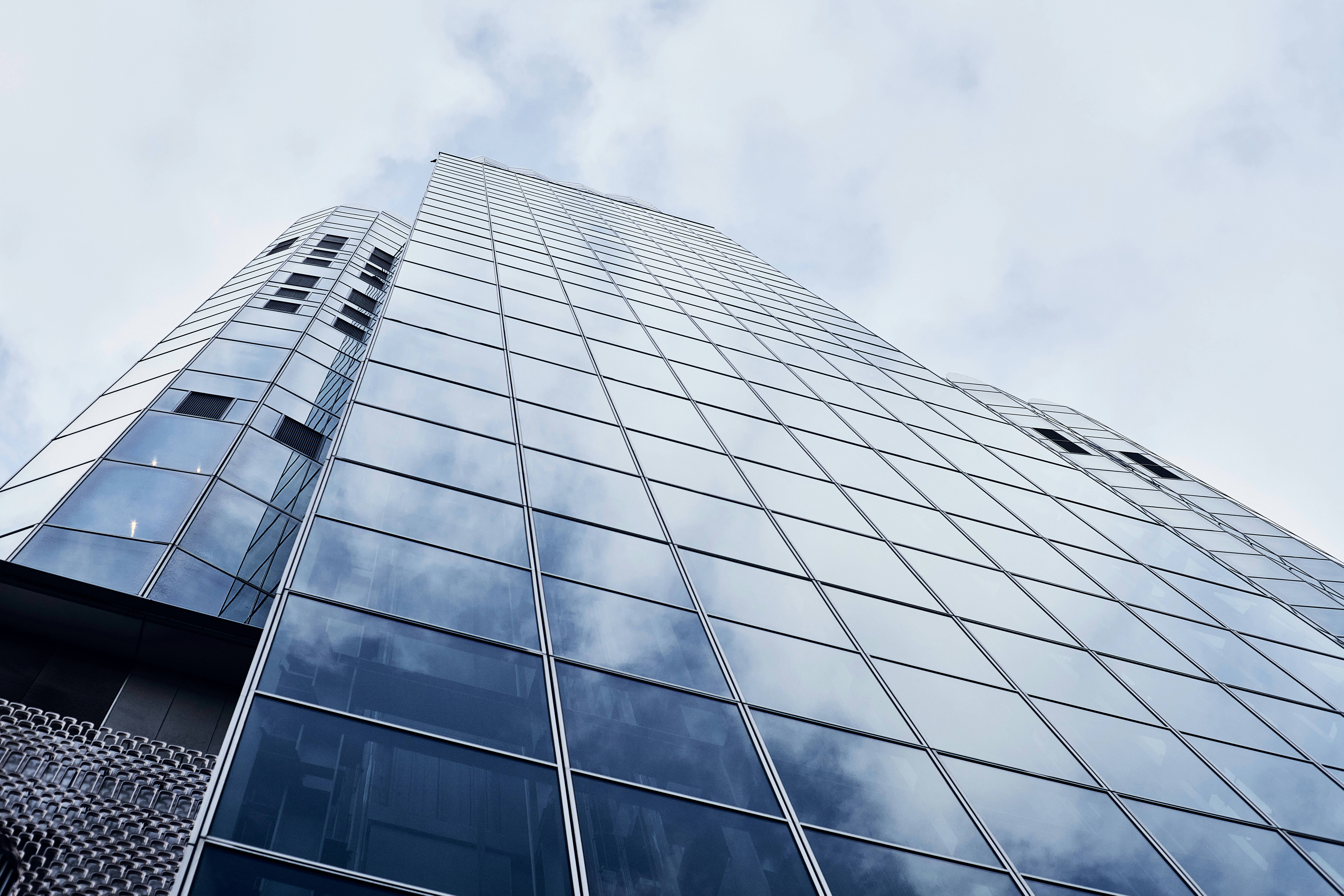 A low angle view of a glass skyscraper reflecting a cloudy blue sky