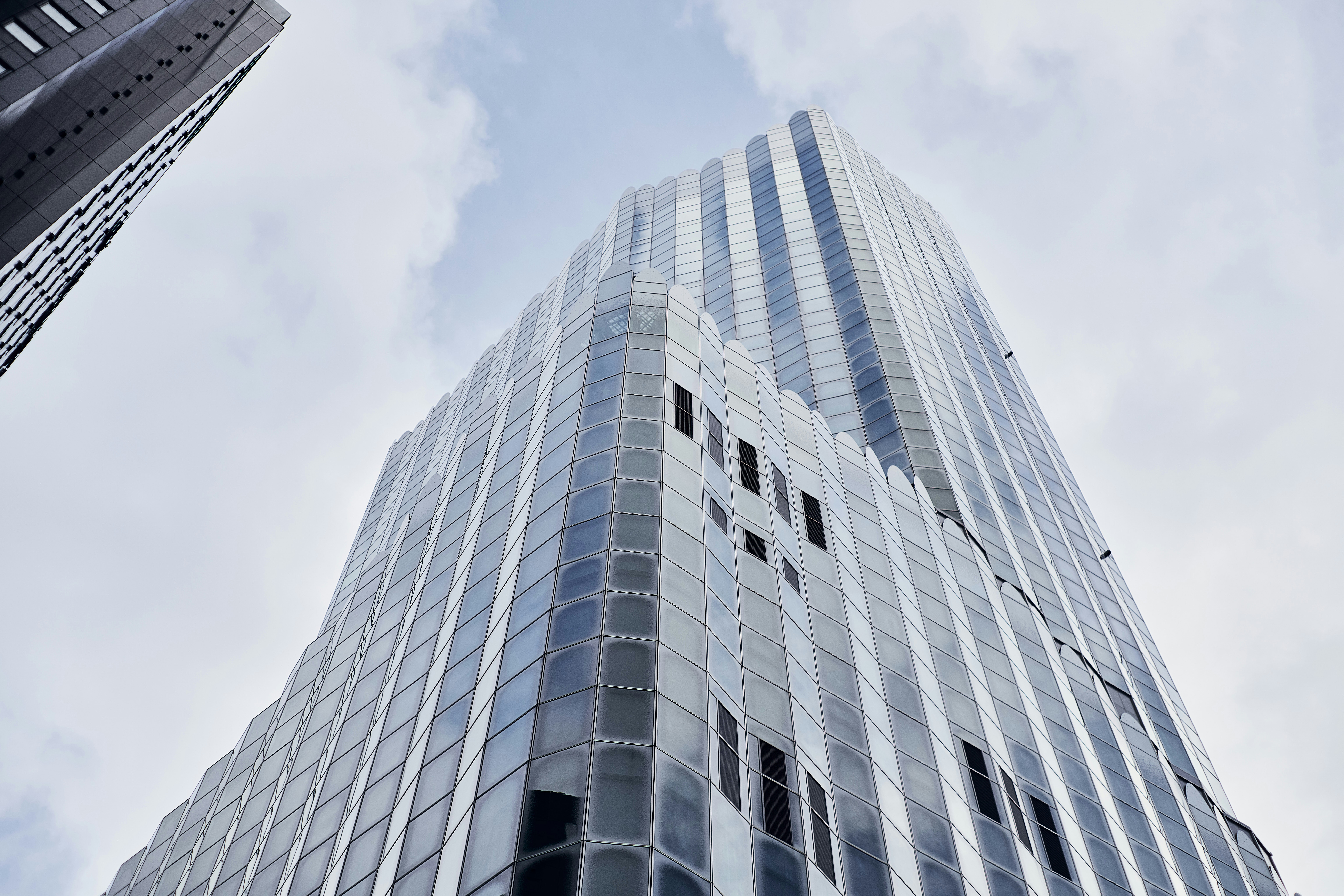 A modern glass skyscraper with a faceted facade against a cloudy sky