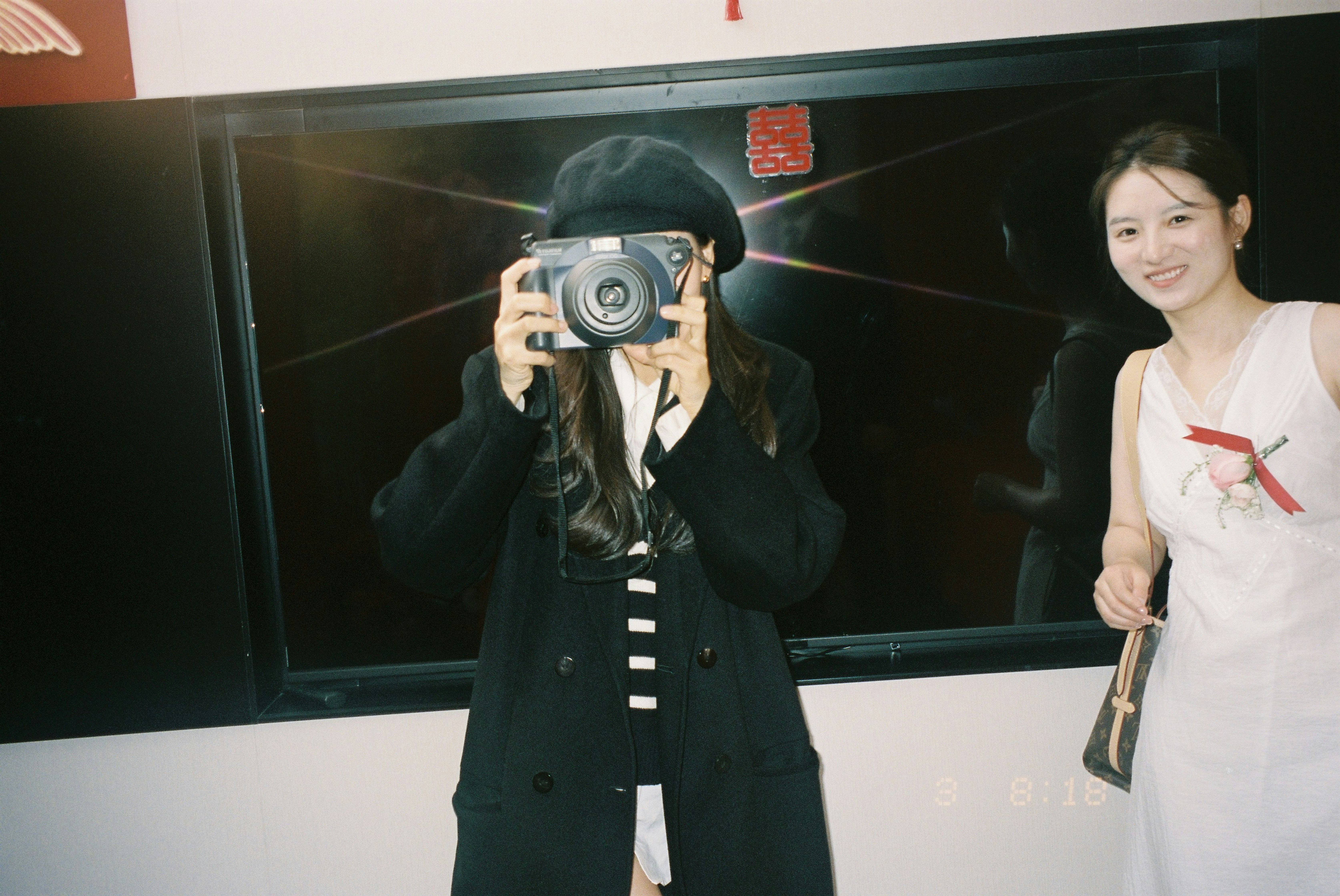A woman holding a camera beside a woman in a white dress