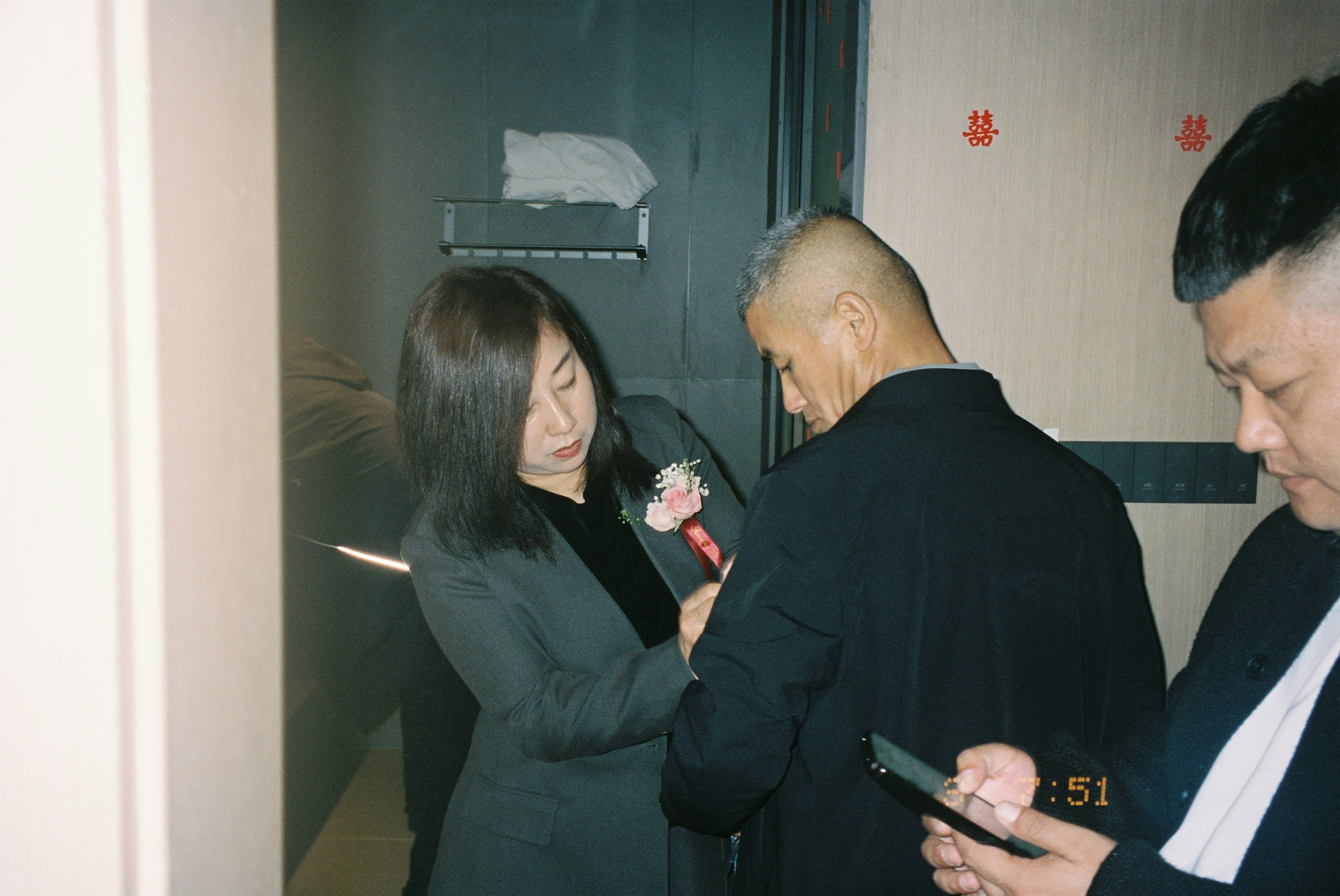A woman in a grey blazer pinning a flower onto a man's jacket