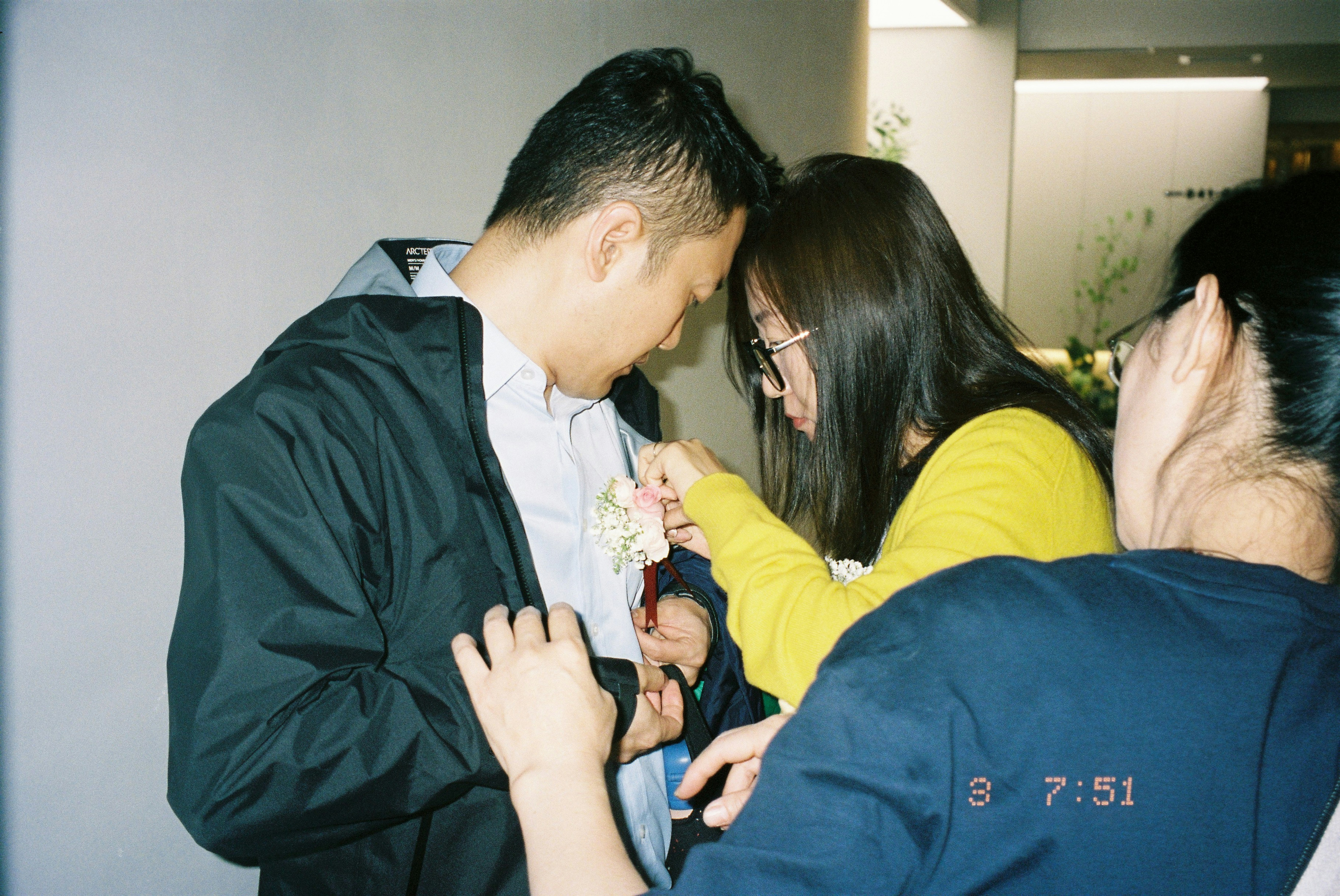 A woman in a yellow sweater pinning a floral boutonniere onto a man's jacket