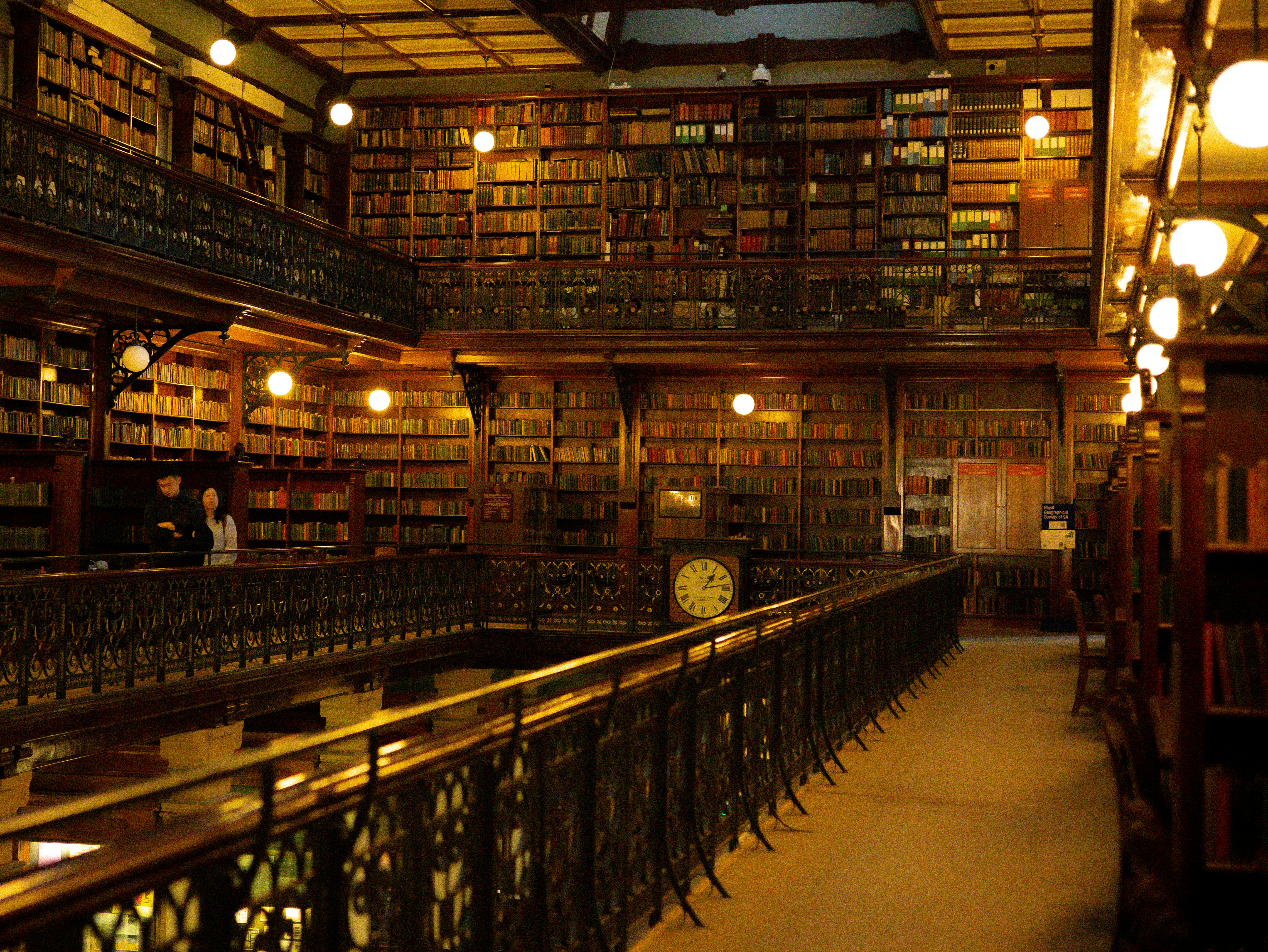 Two people on a balcony overlooking a multi-level library with wooden bookshelves