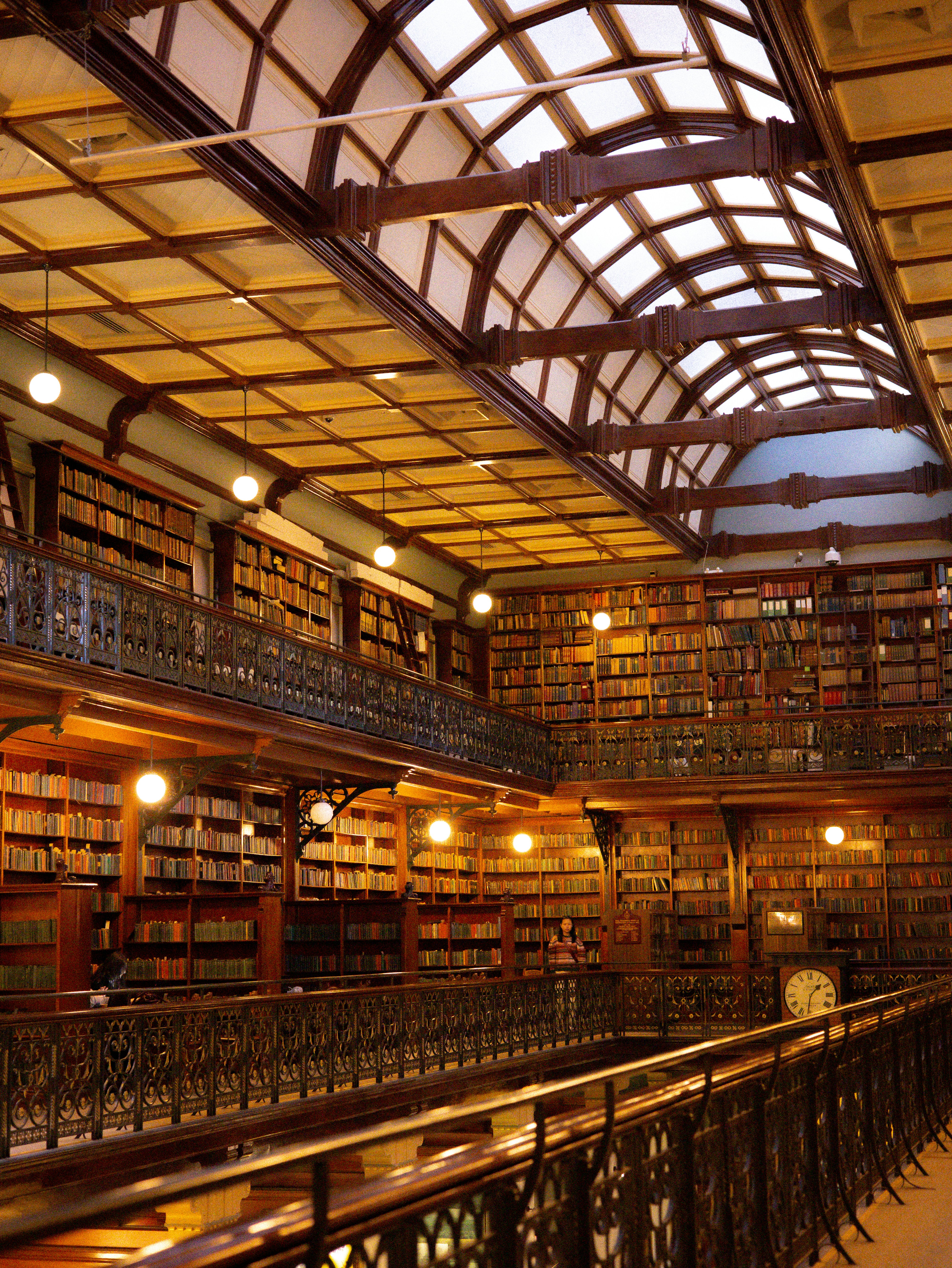 A multi-level library with wooden bookshelves, arched ceilings, and ornate metal railings