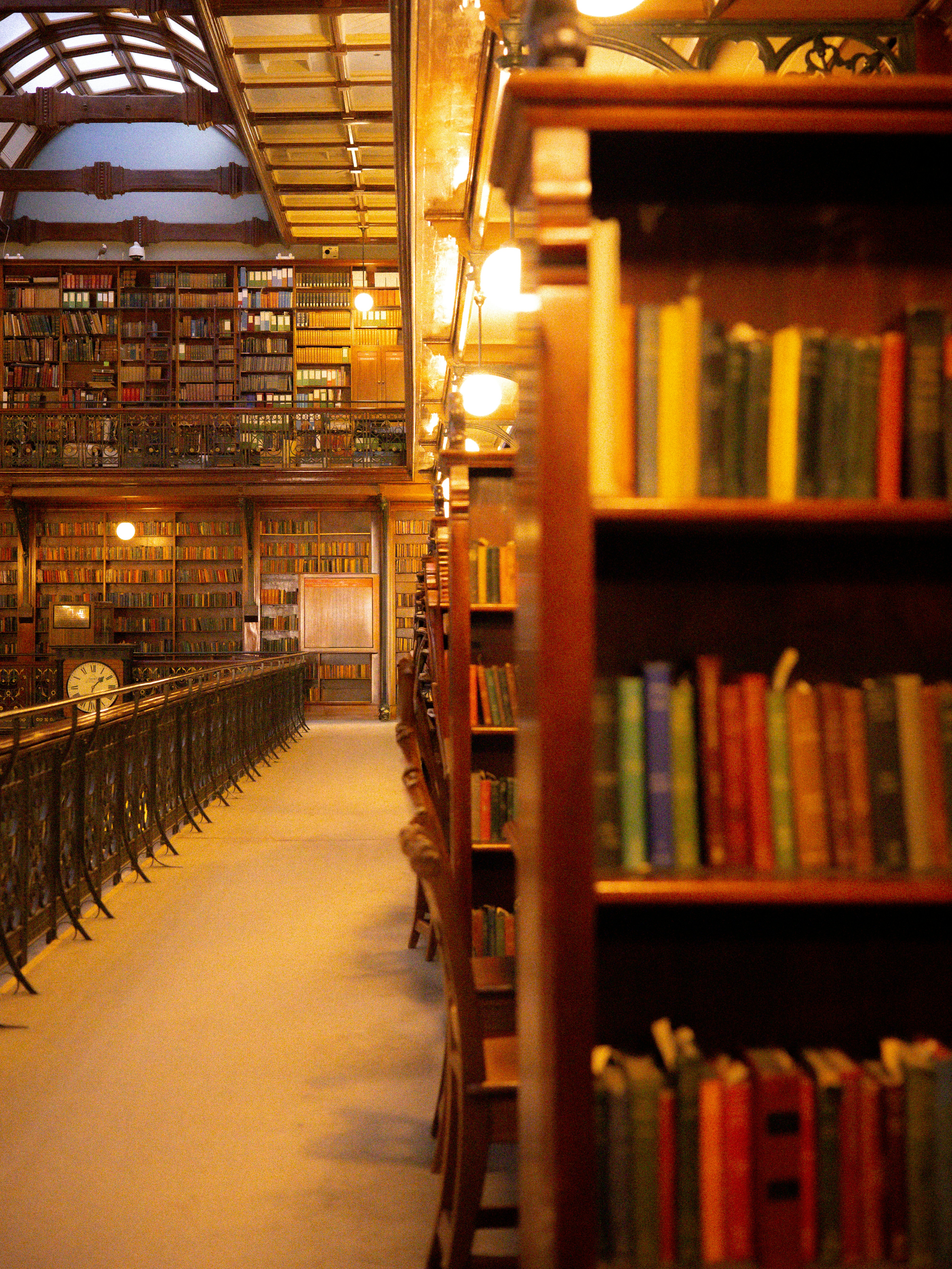 A multi-level library with wooden bookshelves and a metal railing under warm lighting