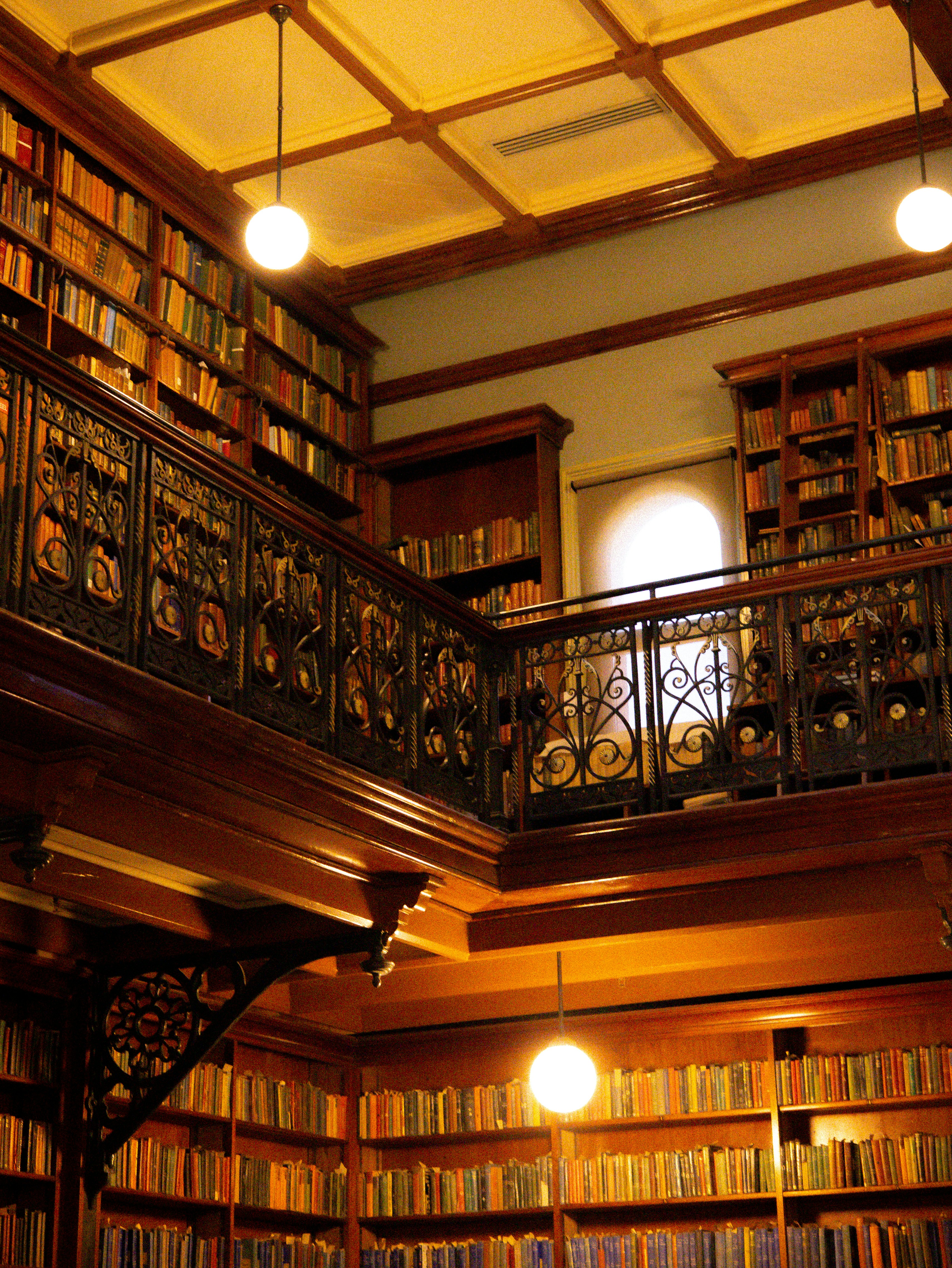 A two-story library with wooden shelves, books, and ornate black metal railings