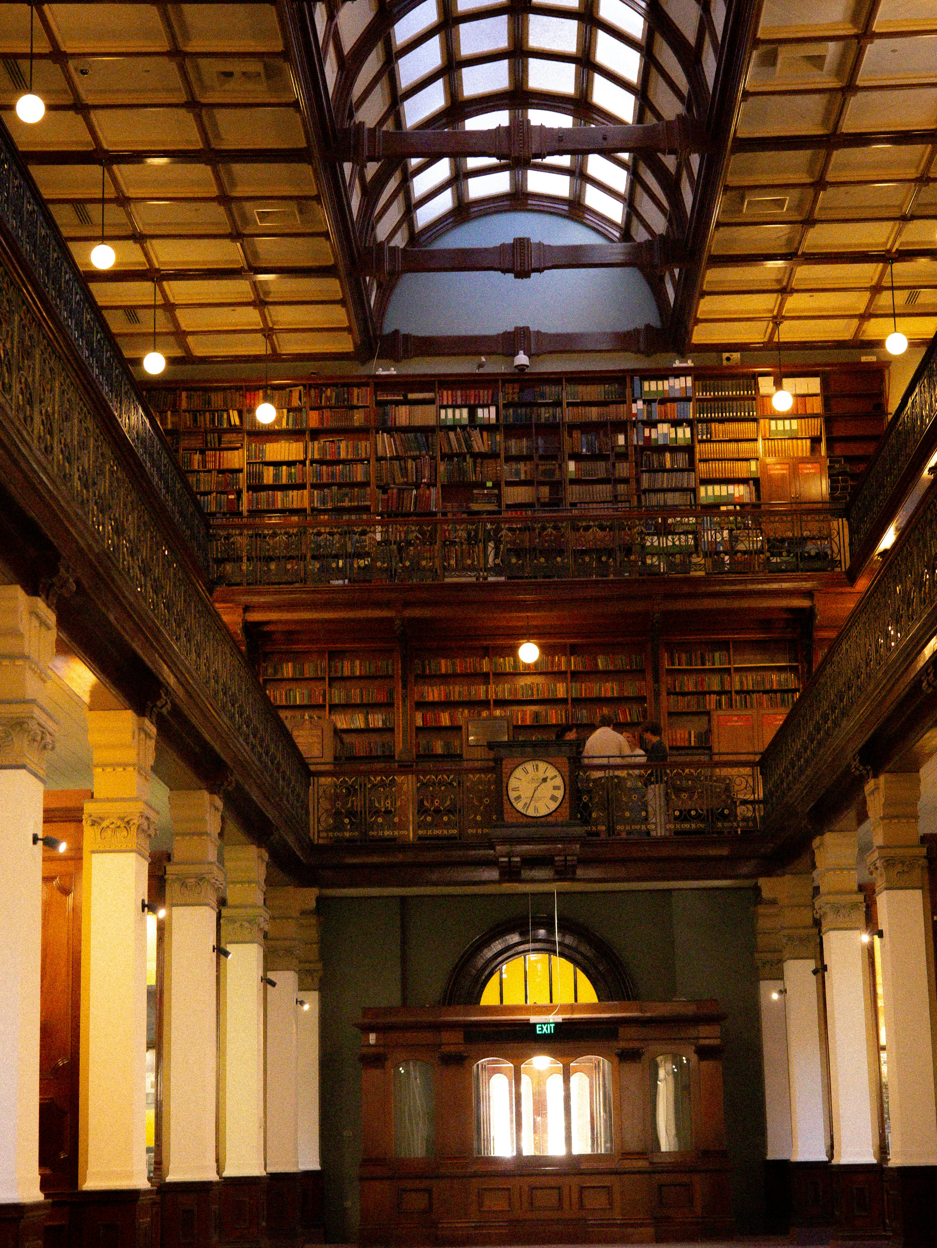 A multi-level library with wooden bookshelves, a vaulted ceiling, and a central clock