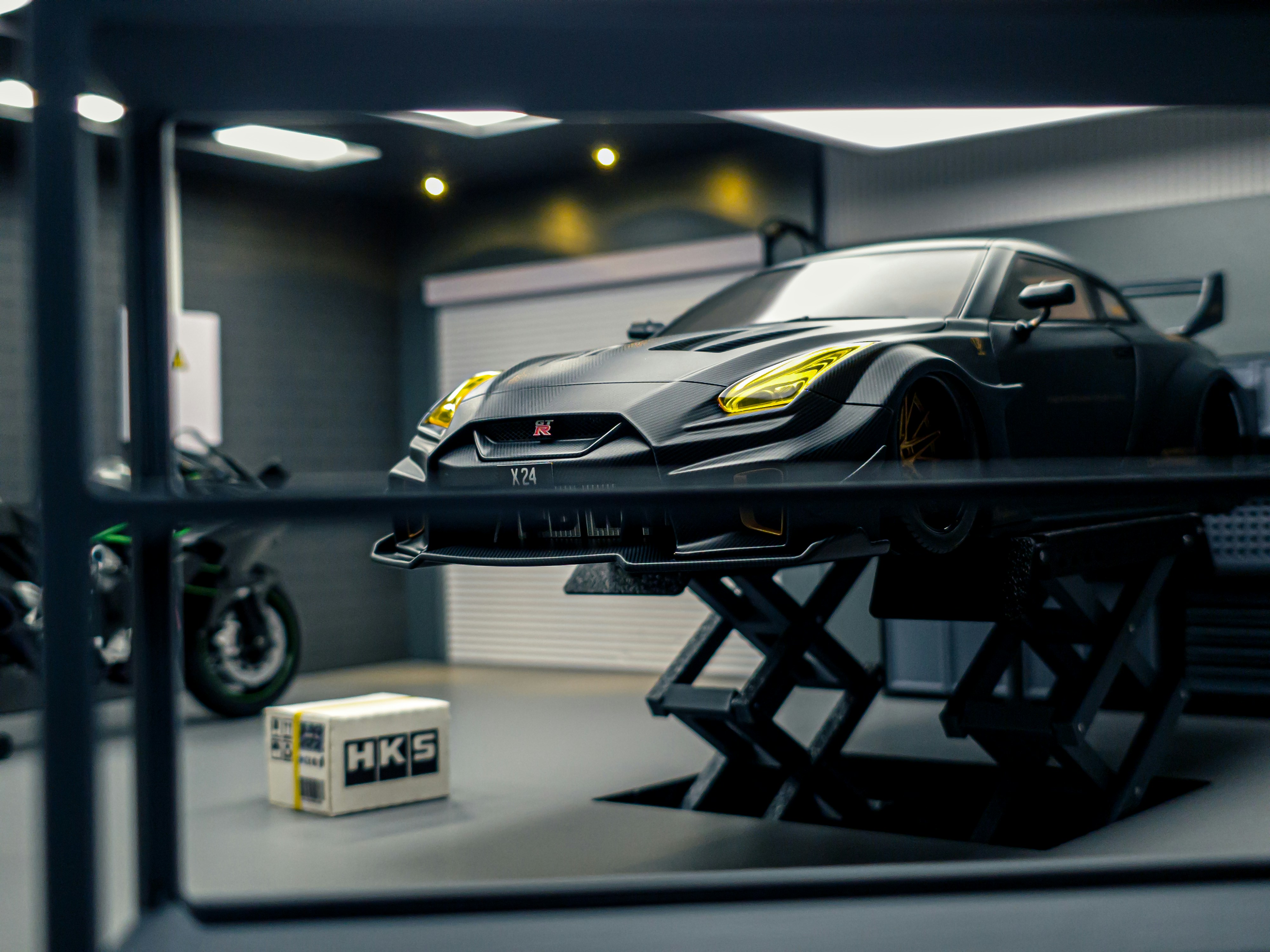 A black sports car on a hydraulic lift in a garage with a motorcycle