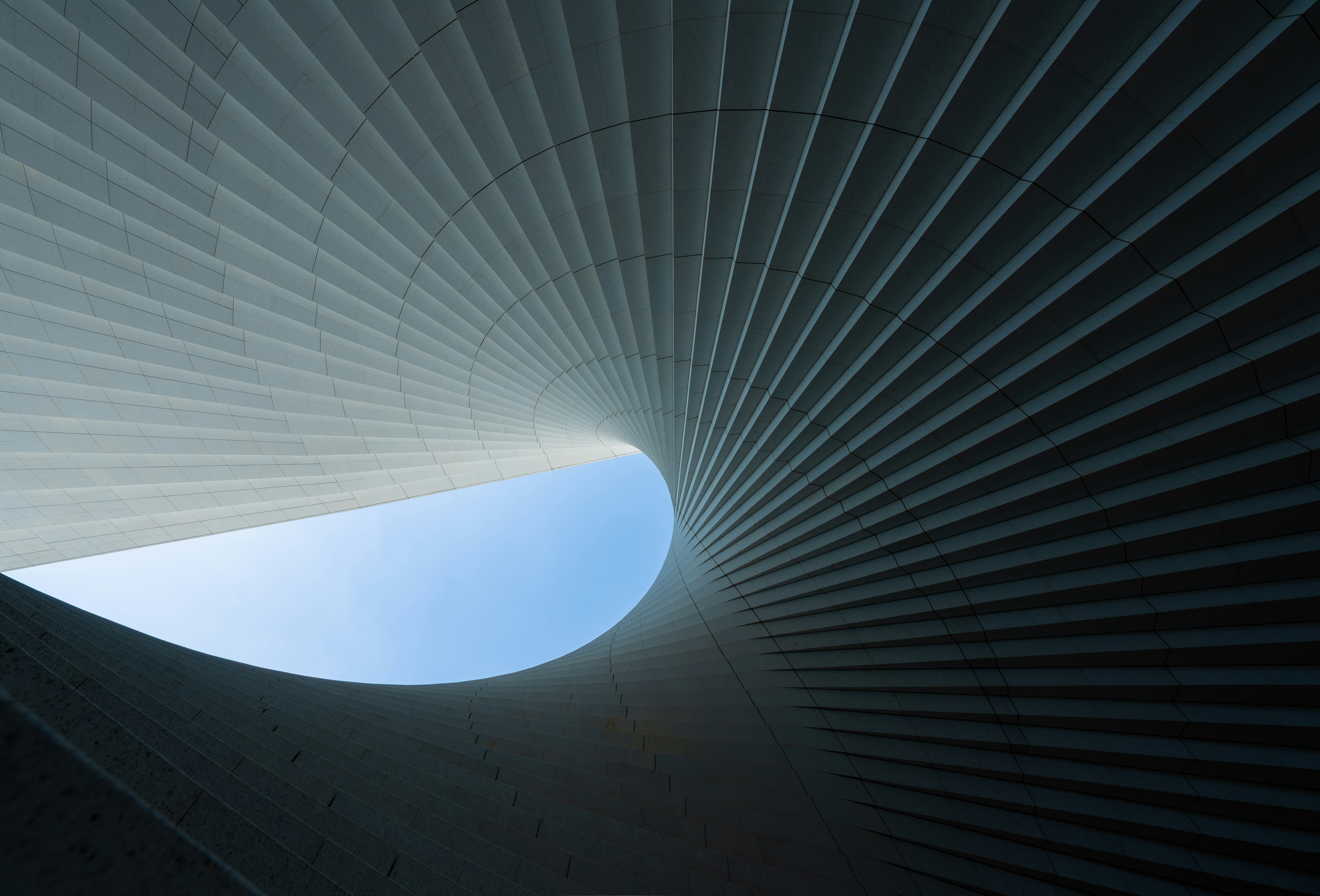 Curved white architectural panels forming a spiral tunnel with a blue sky opening