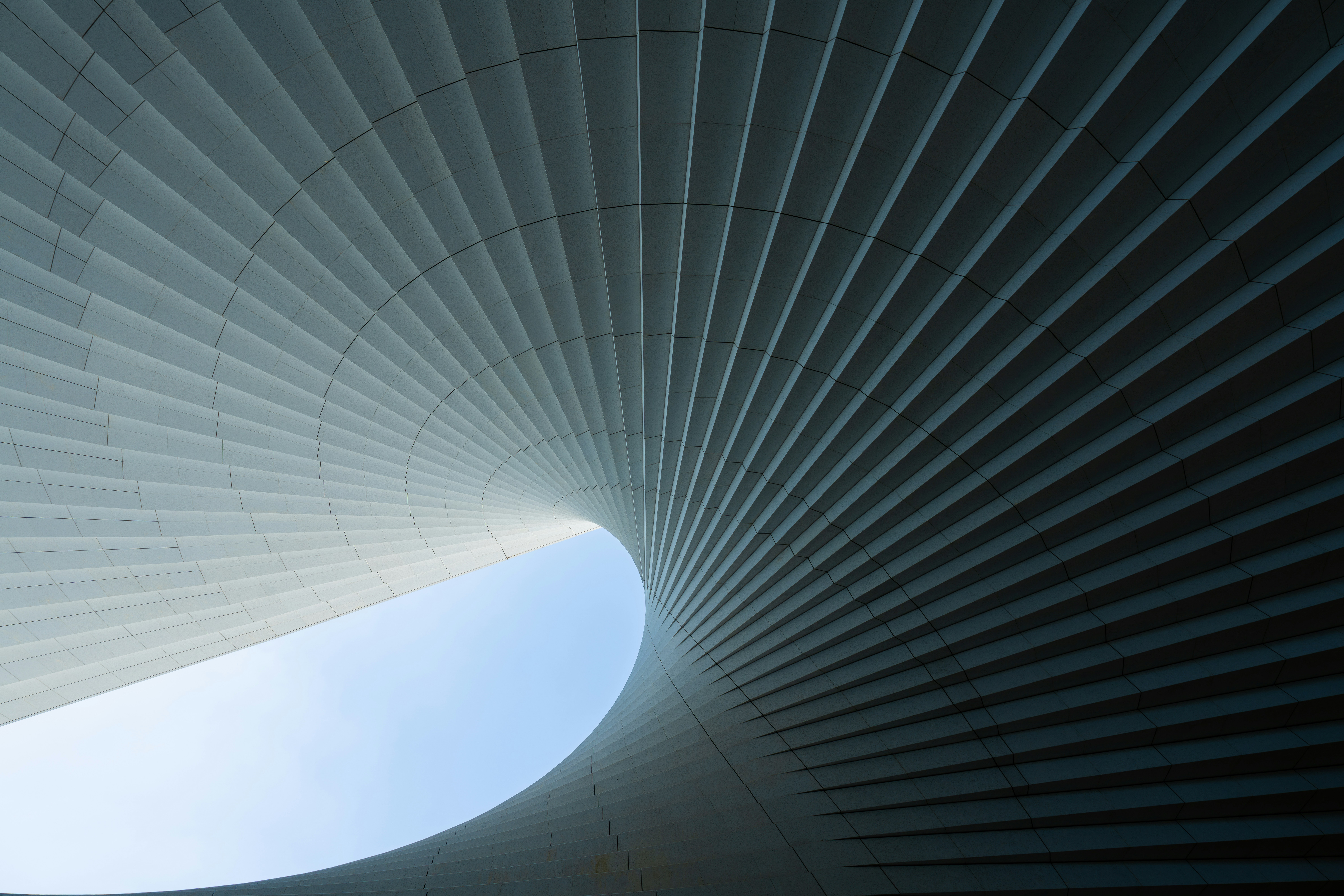 A curved architectural structure with repeating white panels framing a patch of blue sky