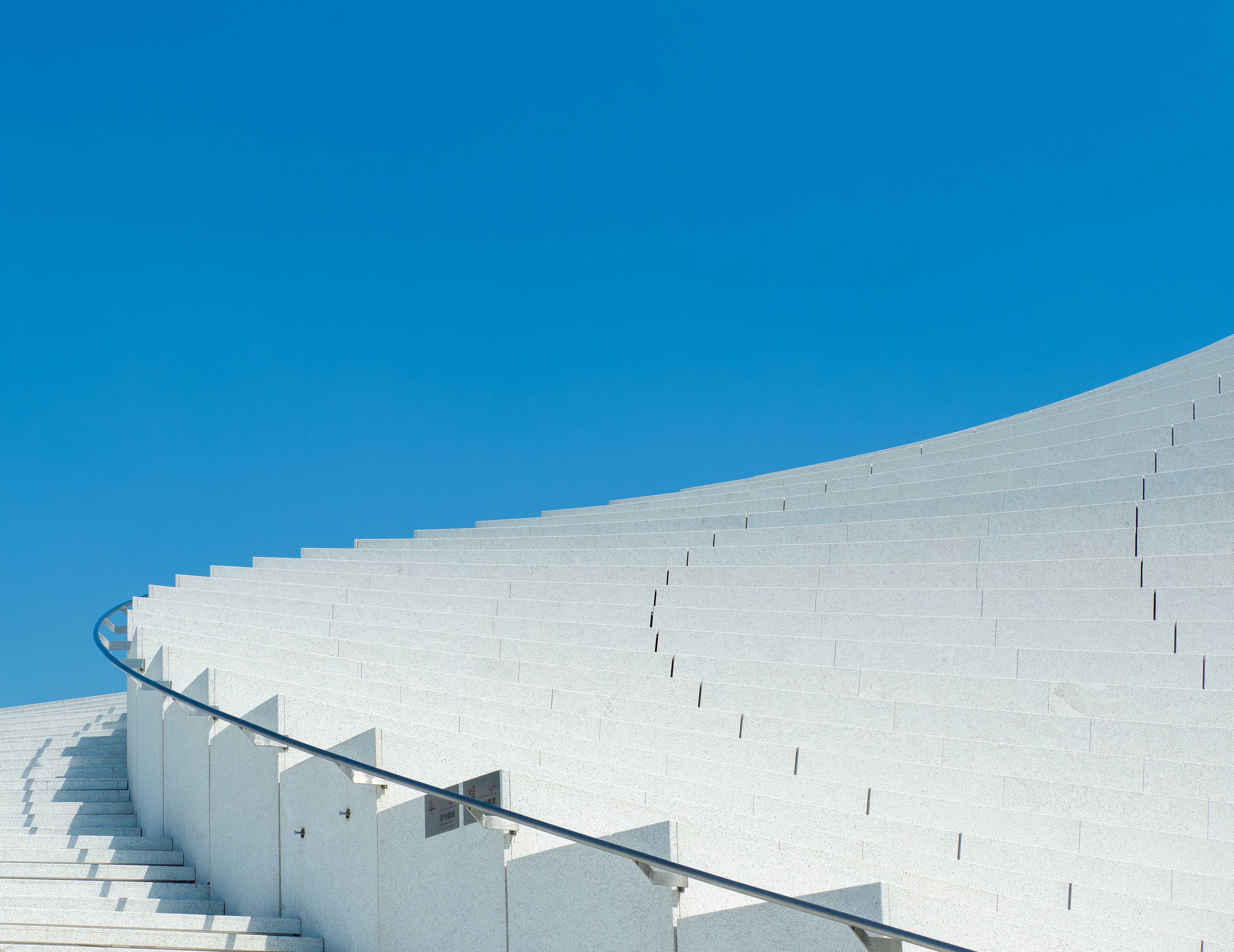 Curved white stone stairs with a metal handrail against a clear blue sky