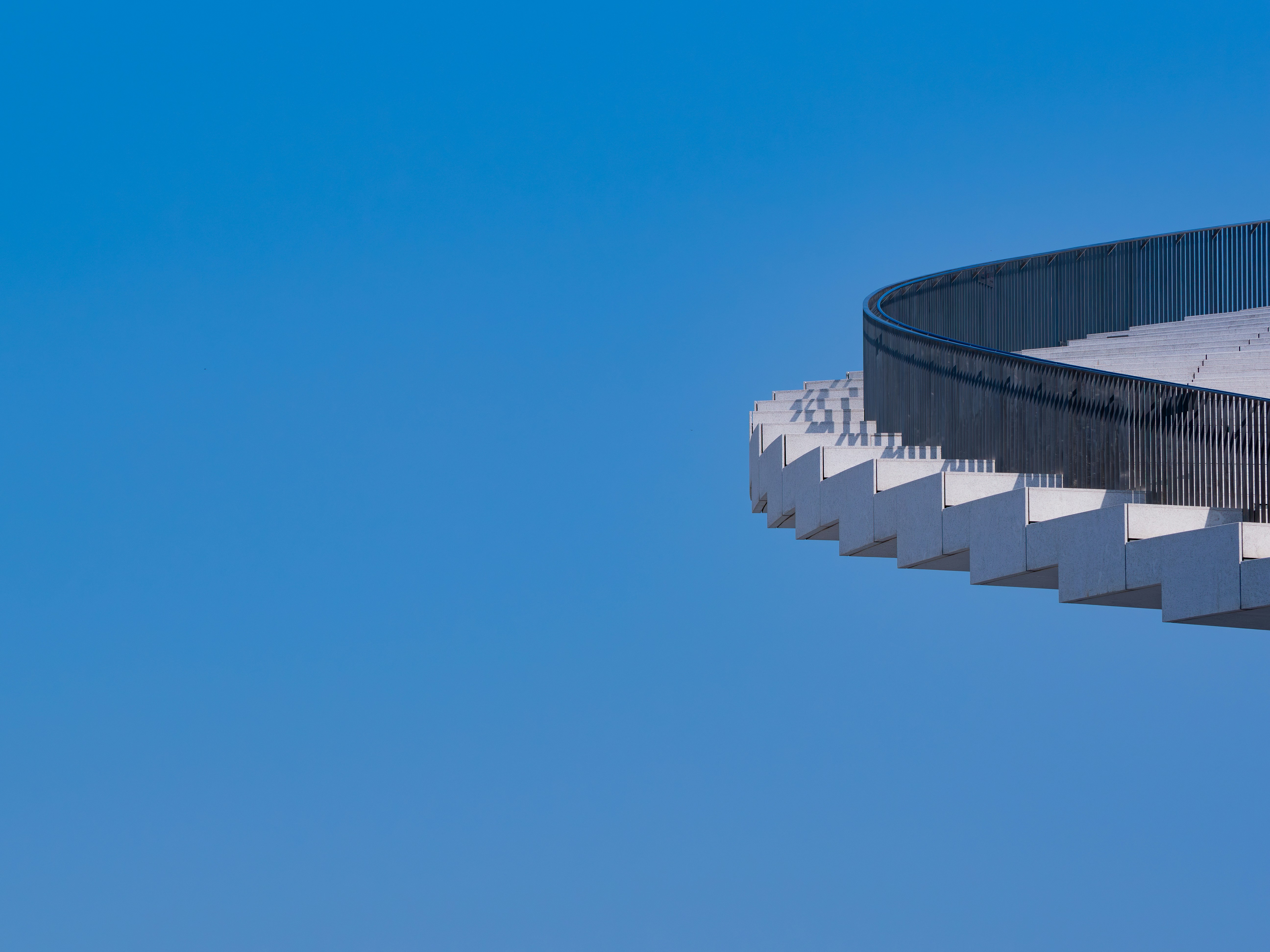 A curved concrete staircase with a dark metal railing against a clear blue sky